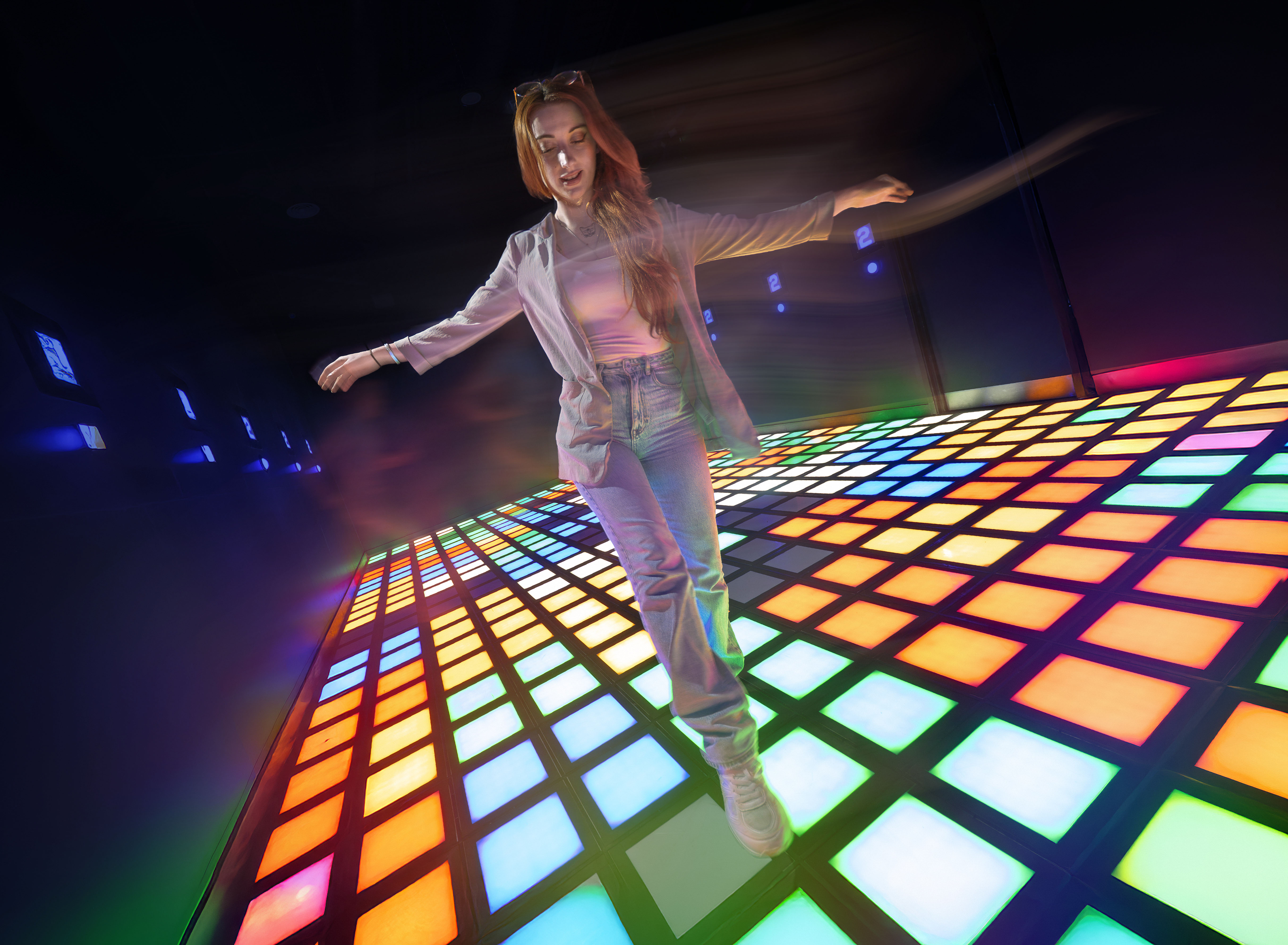 Woman walking on colorful, illuminated dance floor.  The floor is made of square tiles in various colors.