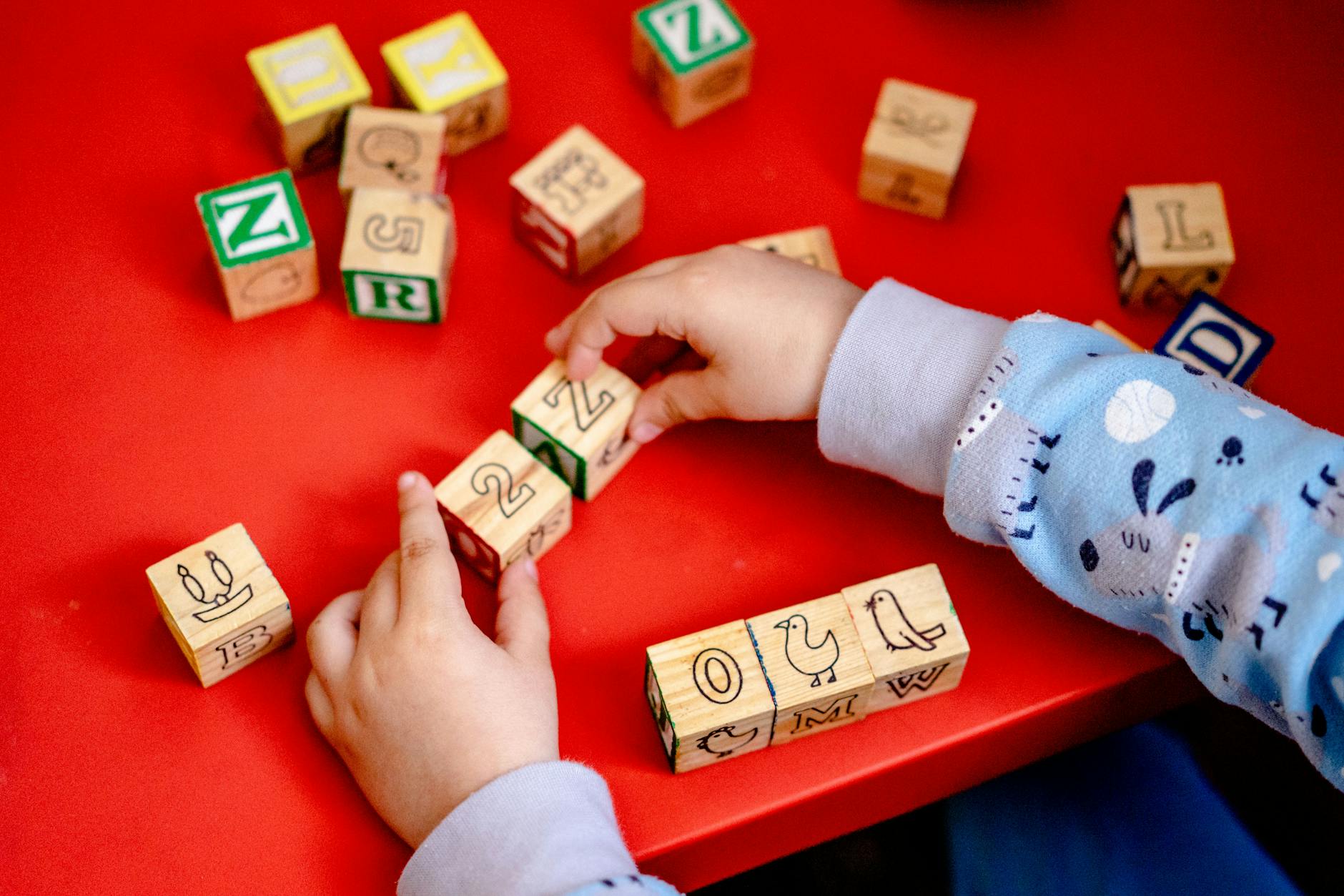 A young student building a complex structure using colorful wooden blocks and geometric shapes on a classroom floor.