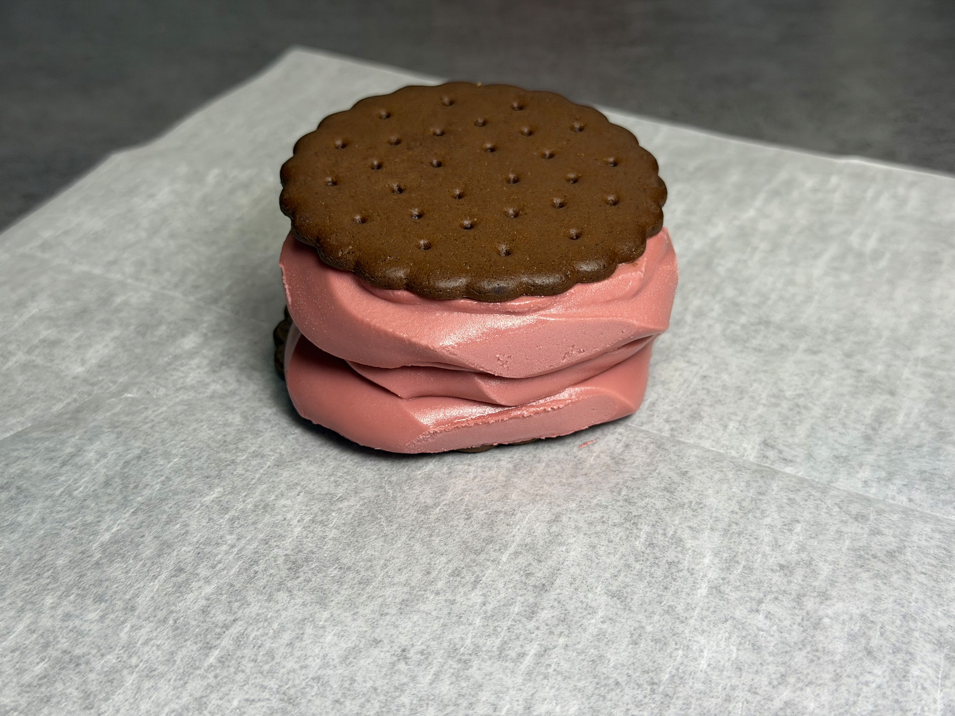 A pink creemee pressed between two chocolate wafer cookies