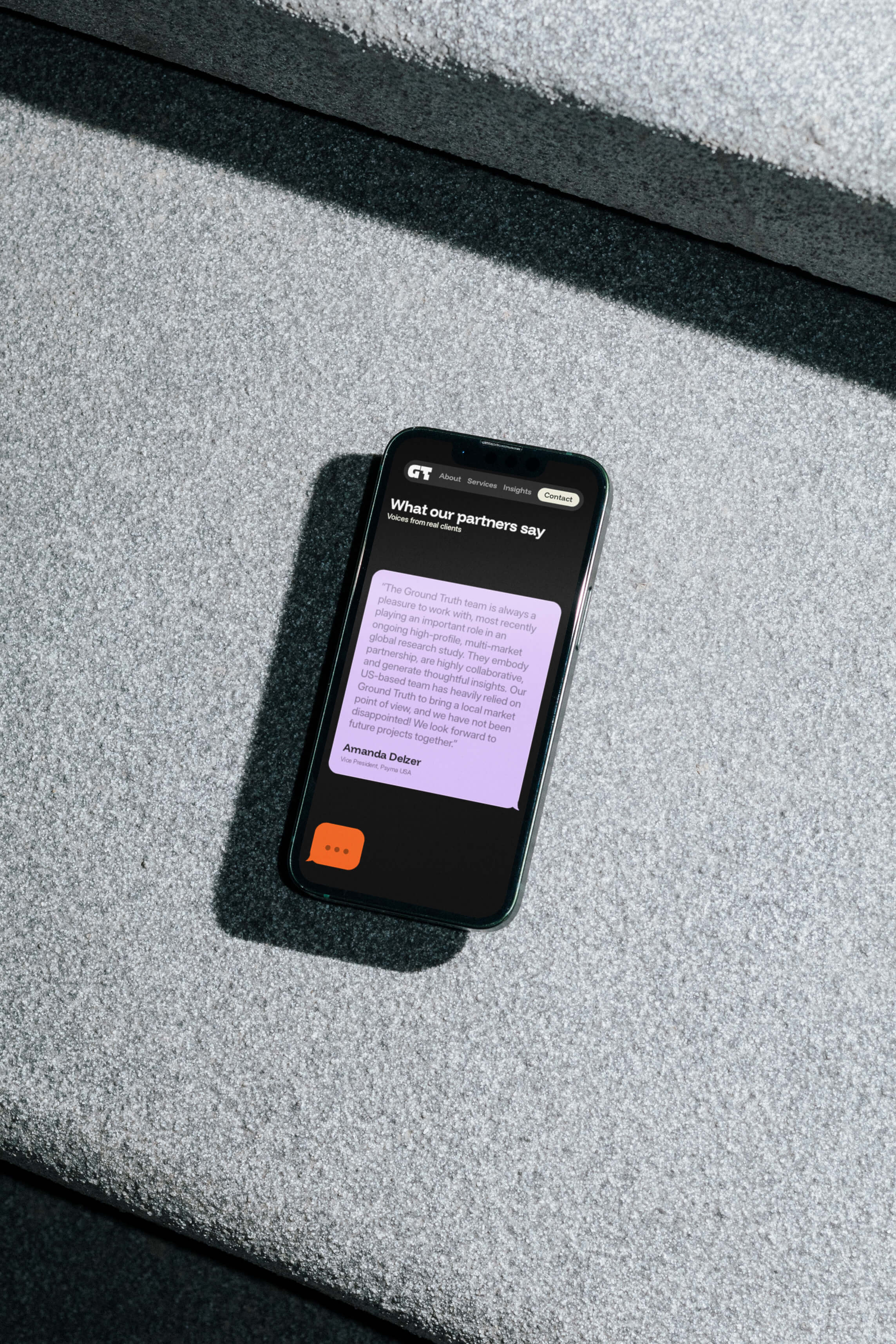 A smartphone lies on a surface, displaying a faint purple screen, with a dark case surrounding it.