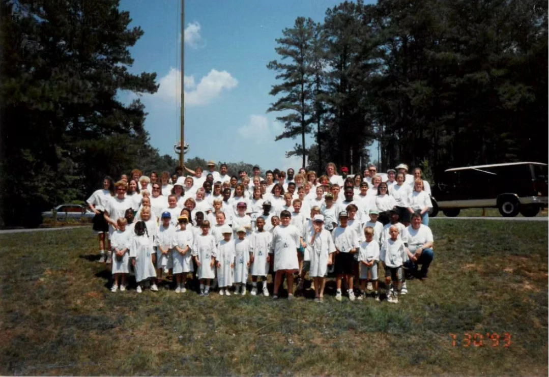 Large group of campers and staff wearing white Camp Juliena shirts, posing for a photo outdoors.