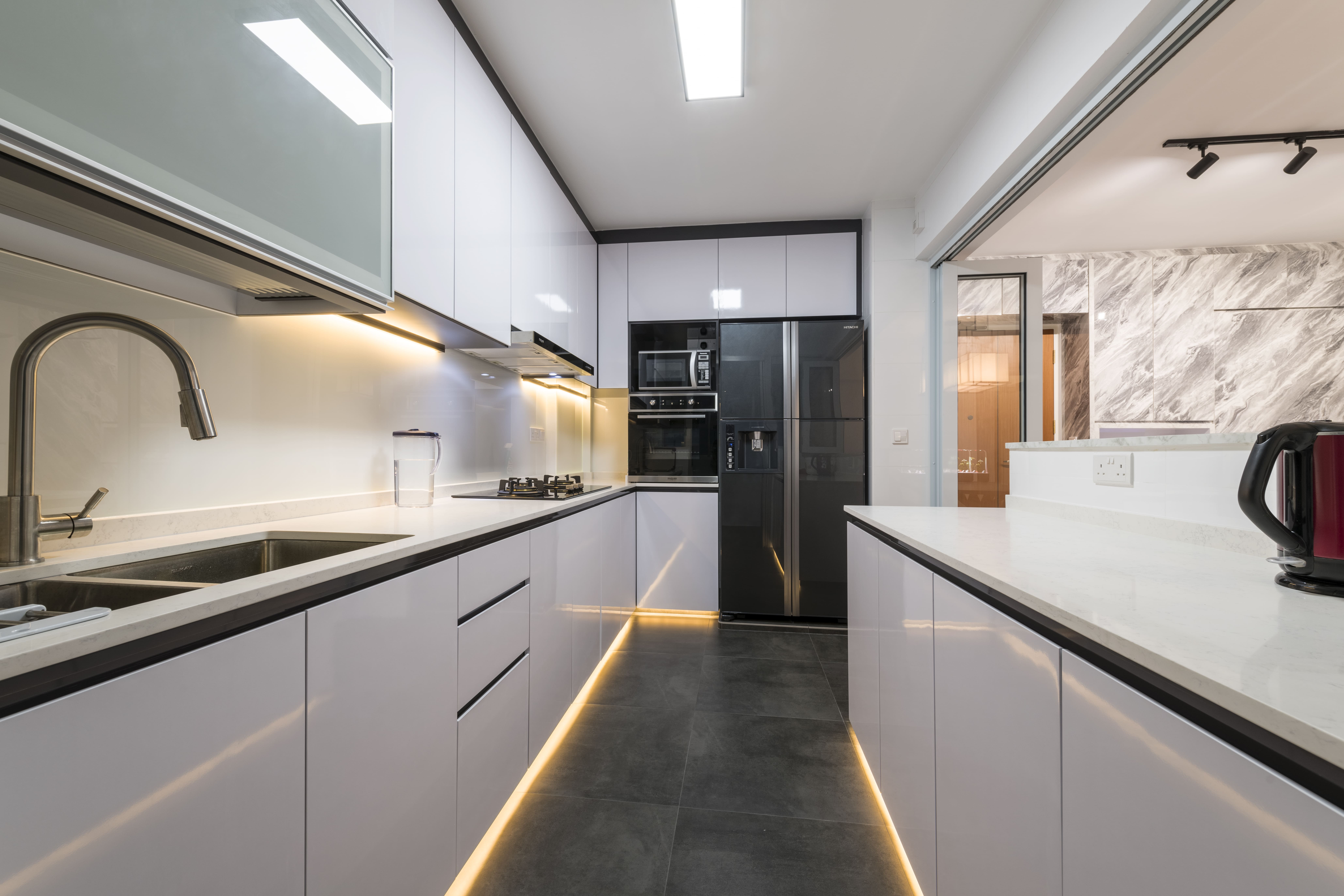 The galley kitchen pairs glossy white cabinetry with under-cabinet lighting and black countertops, combining functionality with a clean, high-contrast finish.