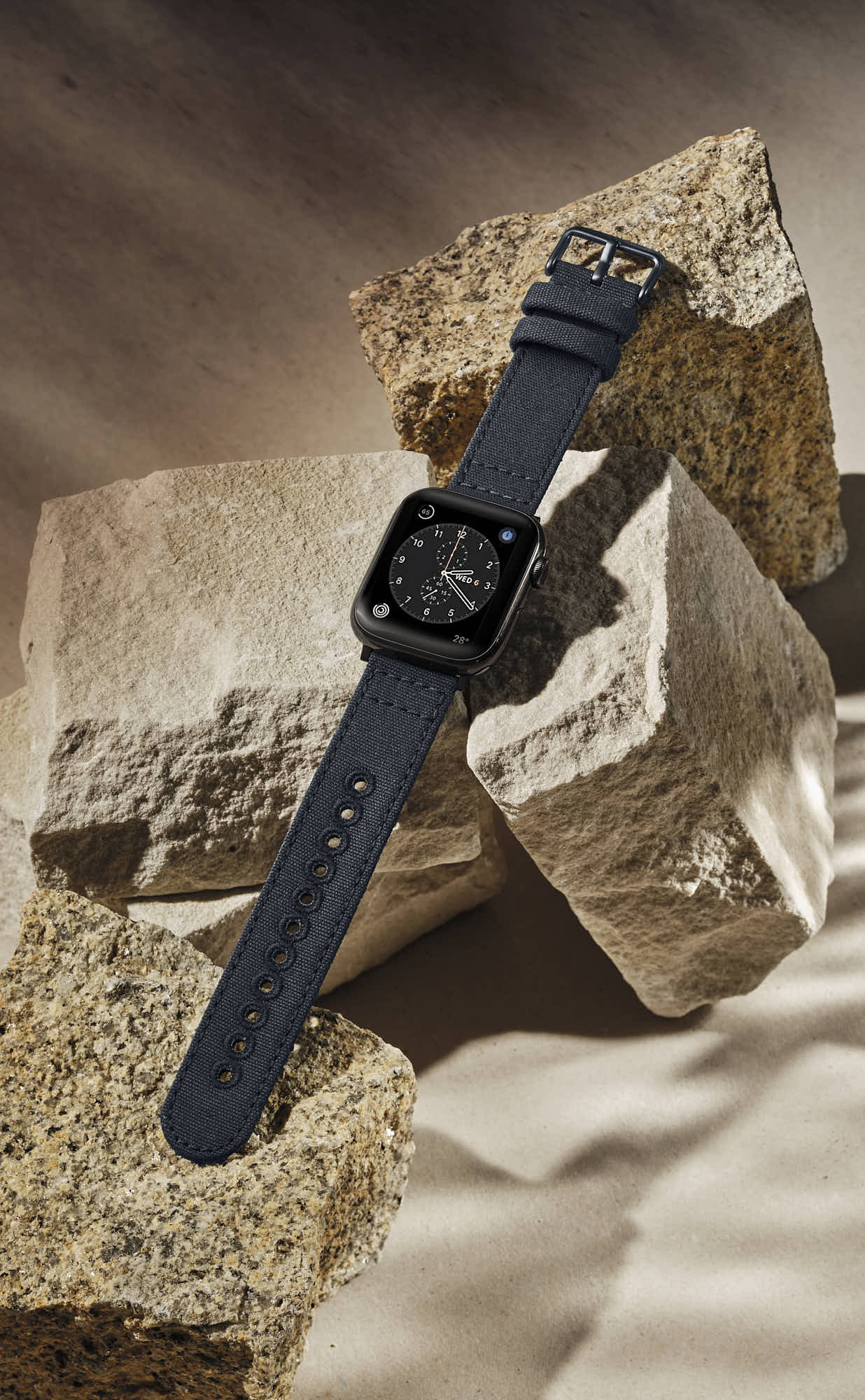 Black smartwatch with navy strap on textured rocks.