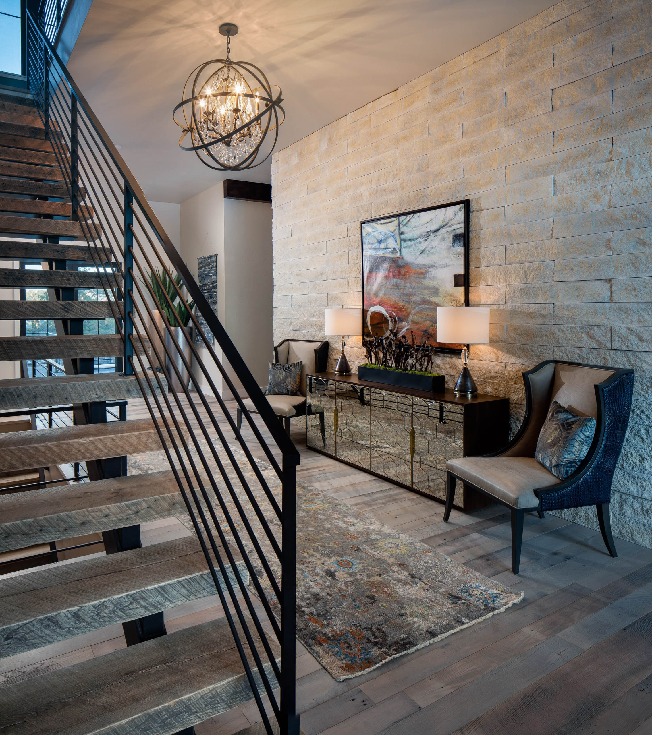 Hallway with modern chandelier, stone wall, and wood staircase.
