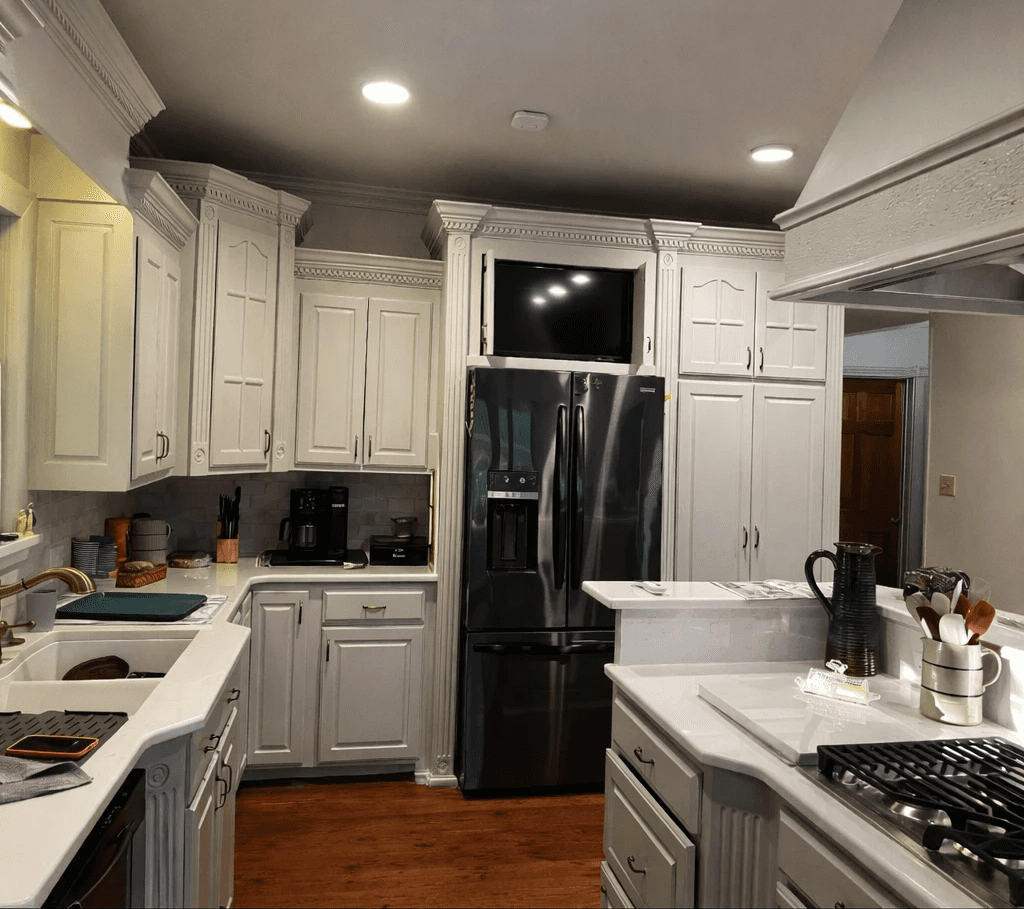 A modern, luxury beachfront villa with large glass windows and balconies overlooks a rocky shoreline, surrounded by palm trees at sunset.