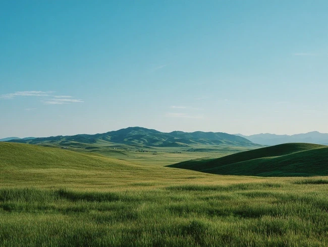 Rolling green hills stretch toward a distant mountain range under a clear, pale blue sky.
