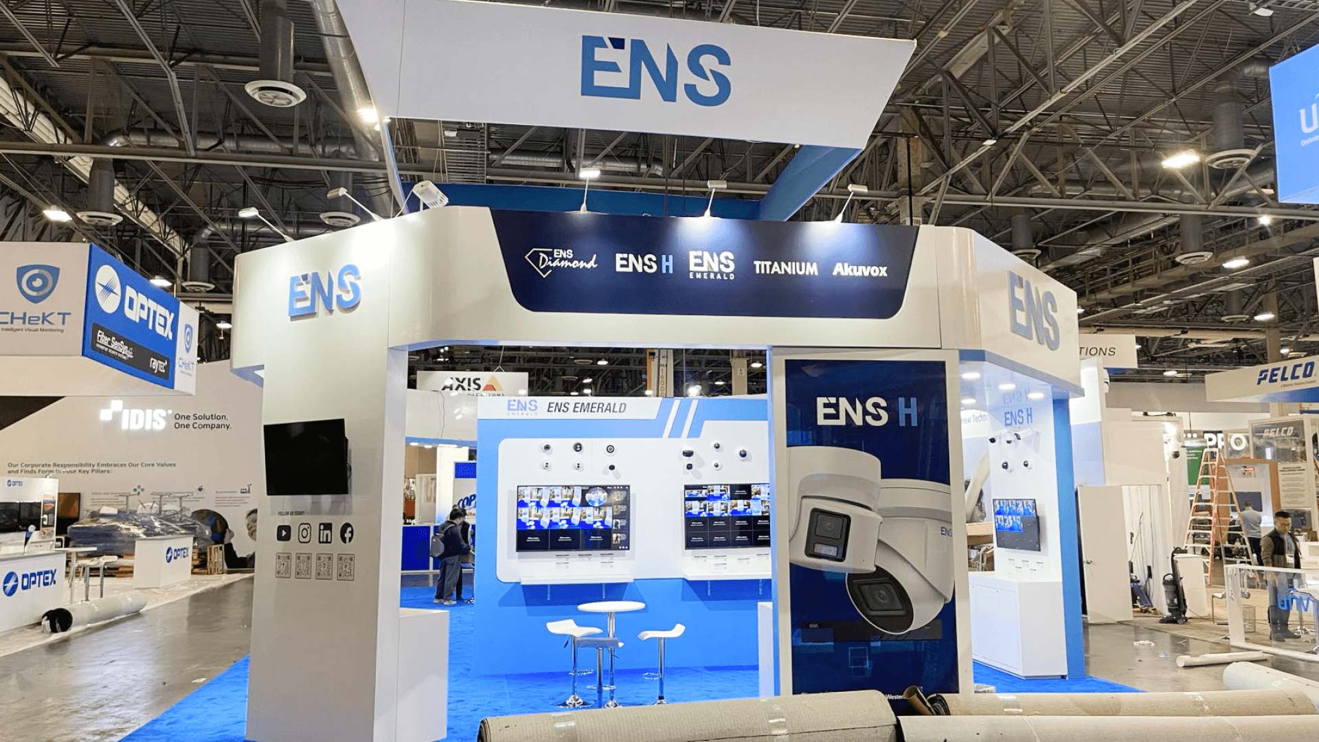 Front corner view of ENS 20x20 island booth showing open entry and blue carpet at ISC West 2023.