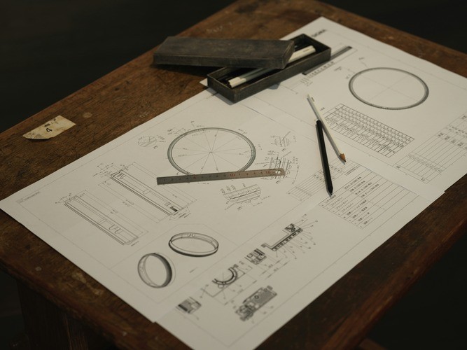 Engineering blueprints on a wooden table with pencil and ruler.