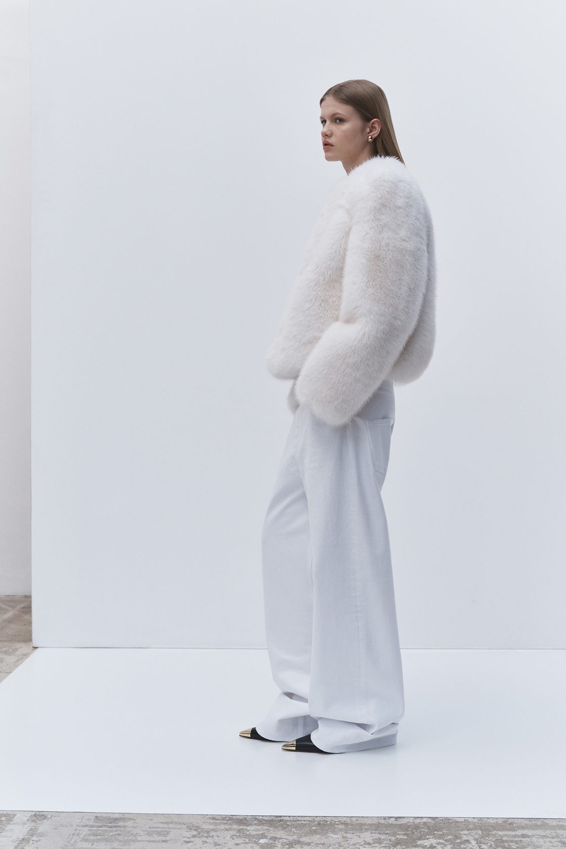 A person with shoulder-length hair is wearing a tiger print sweater and high-waisted black leather shorts, holding a black clutch with a gold accent, standing on sunlit stone steps.