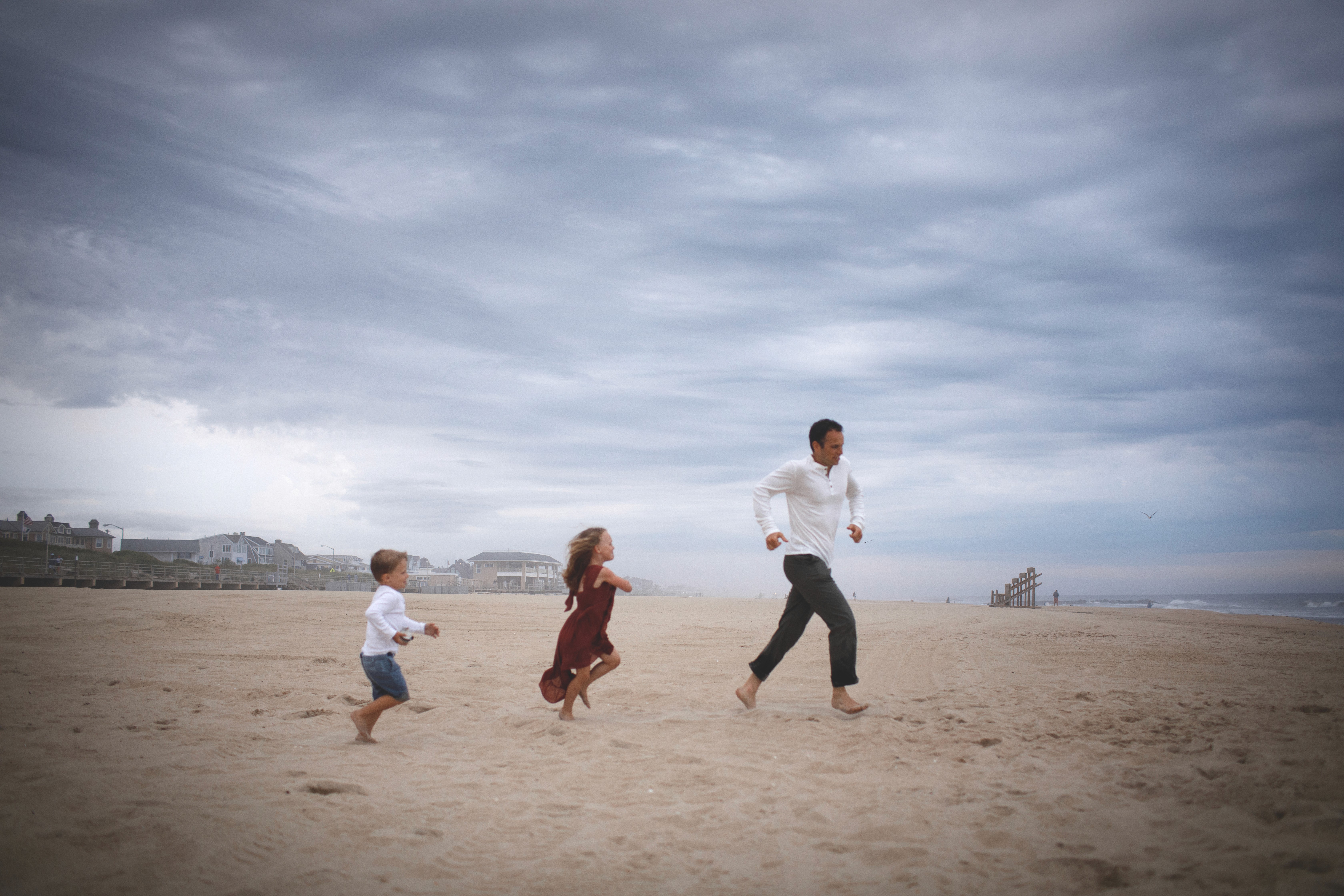 Family holding hands and running along the ocean during a candid moment.