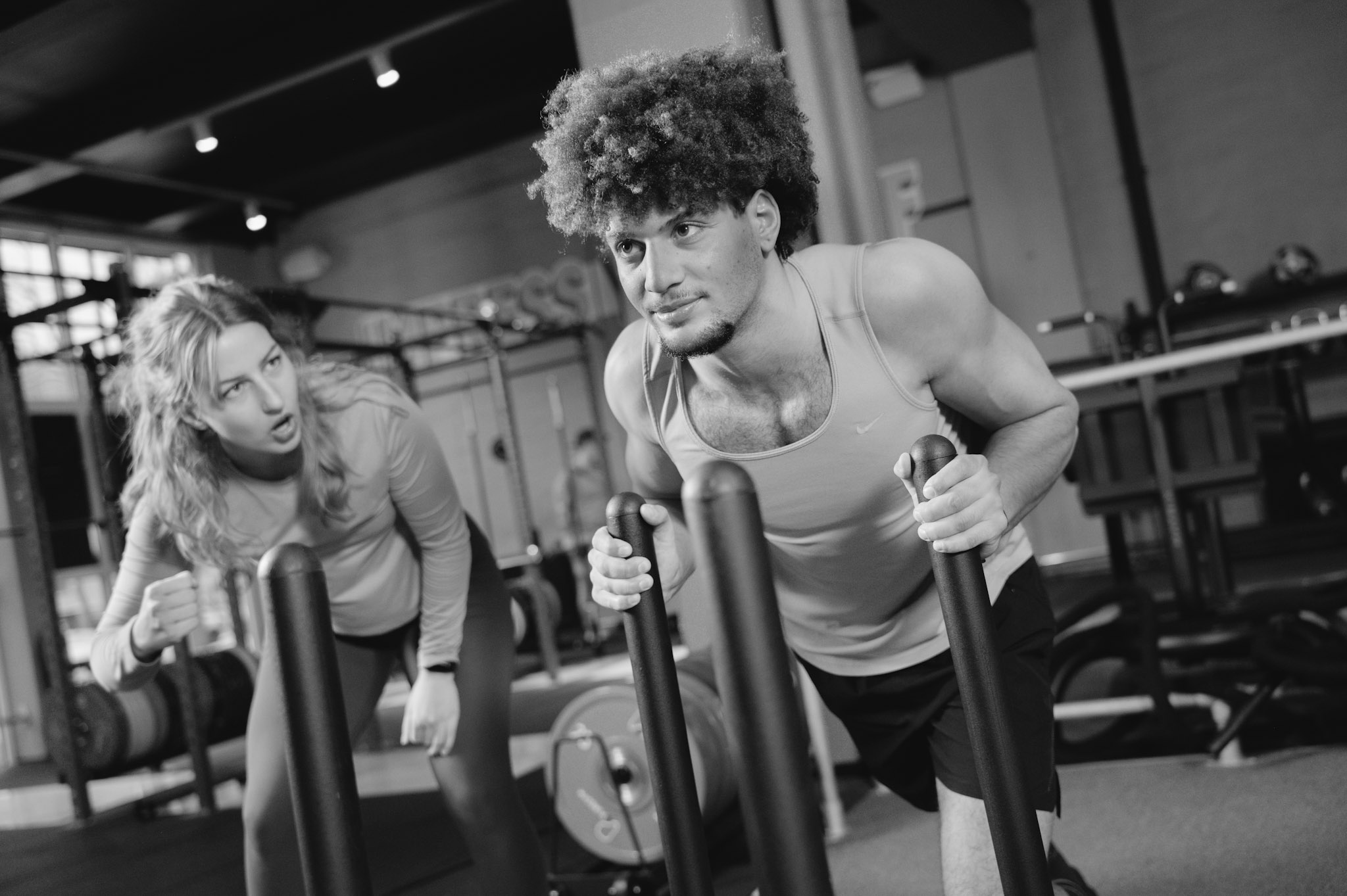 Man pushing weights in a gym with his trainer motivating him. 