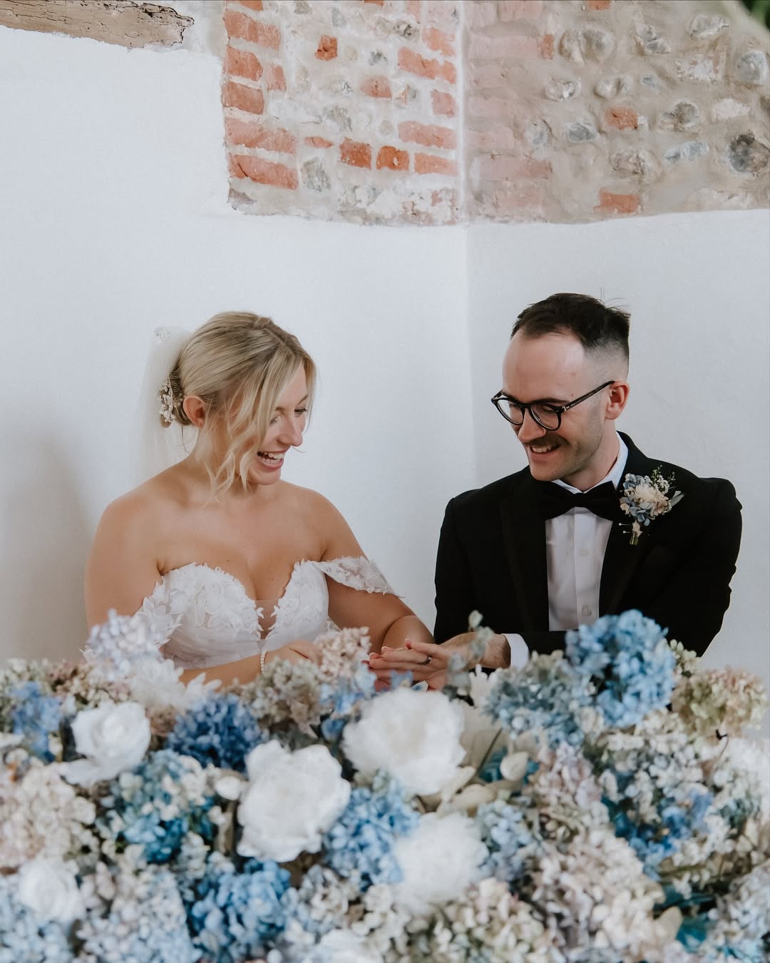Bride and groom exchanging rings, smiling with joy. The couple is at a flower-covered table, celebrating their wedding.