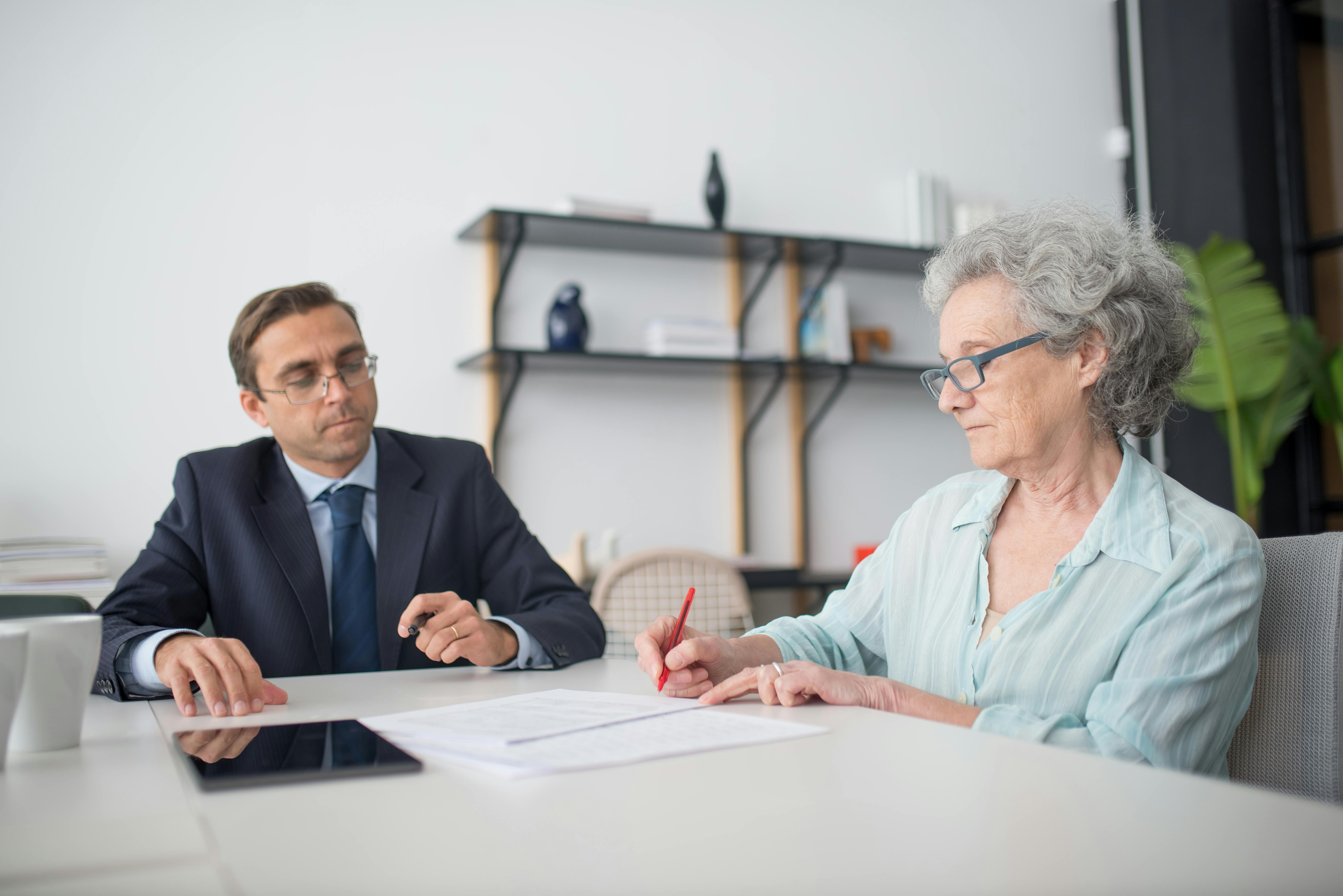 elderly-woman-signing-paperwork-in-modern-office-with-consultant. - kampus-production (pexels)