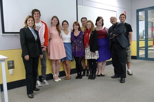 A photo of a group of people standing in a classroom with a projector screen behind them.
