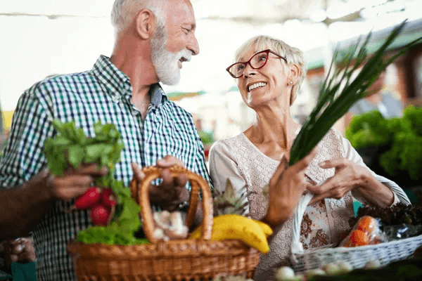 Senior couple shopping with baskets and holding healthy food.