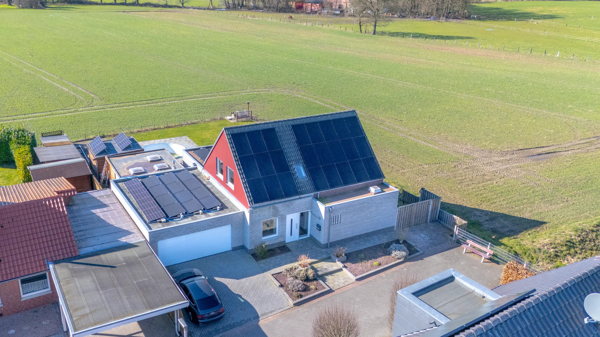 Schrägaufnahme per Drohne eines Einfamilienhauses in Ochtrup mit rotem Giebel, Photovoltaikanlage auf Satteldach und Flachdach-Garage, Vorgarten und angrenzendem Grünland