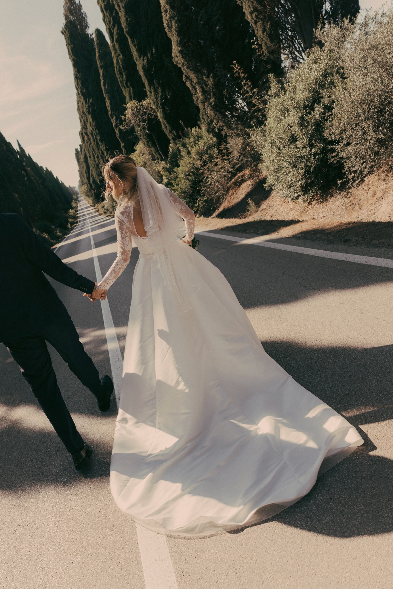 Sposa in abito lungo con velo nel Viale dei Cipressi di Bolgheri, luce dorata al tramonto, reportage matrimoniale
