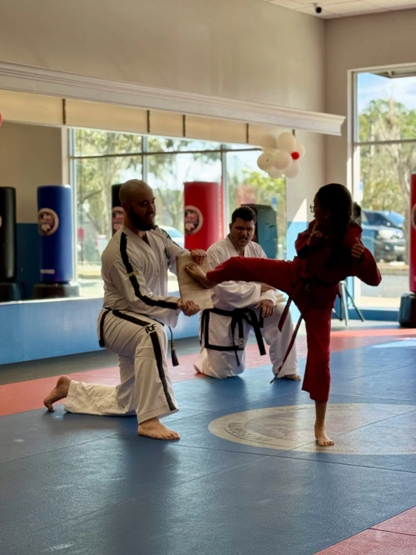 Instructor holding a board as a student attempts to break it with a kick.