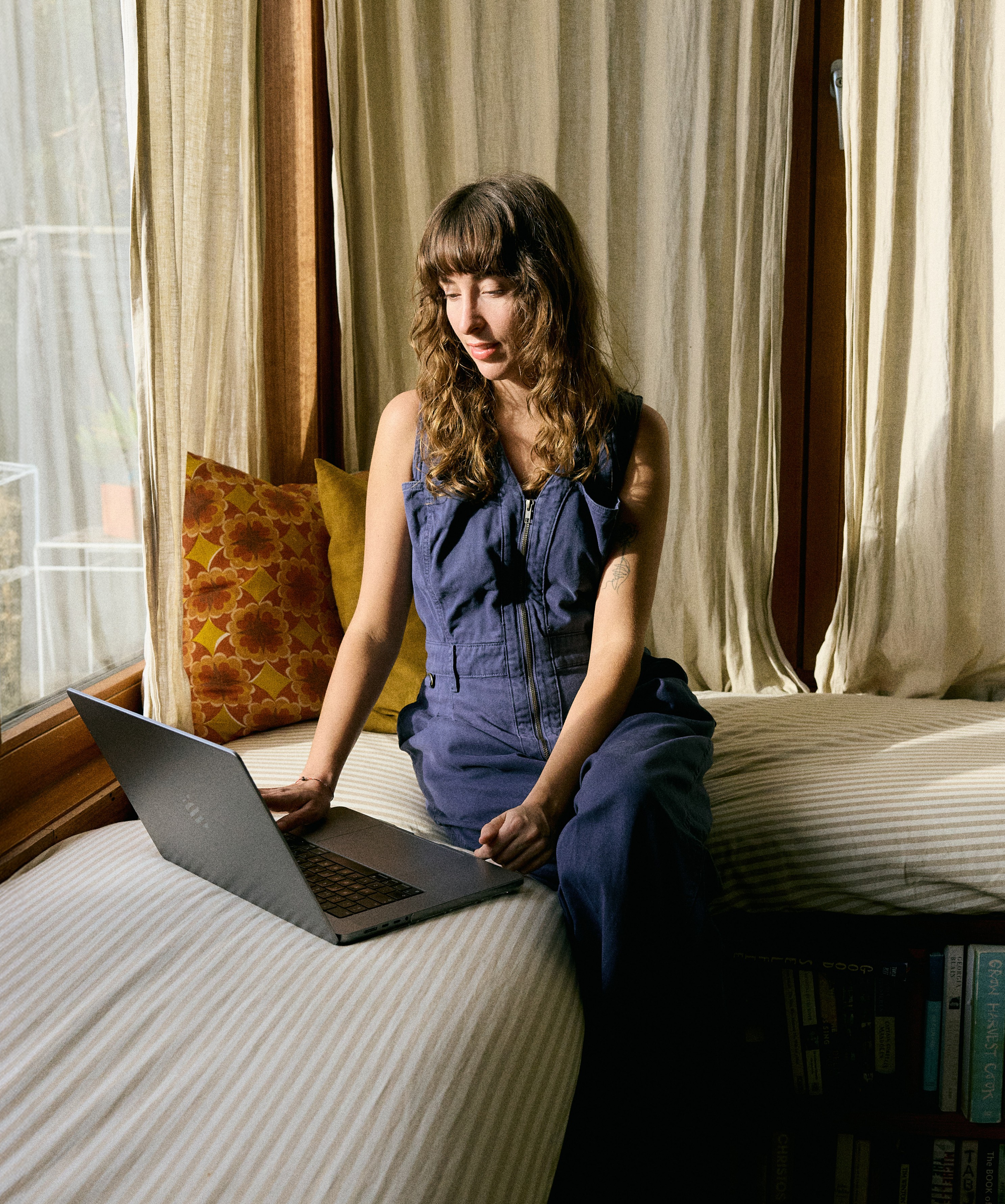 Woman in blue jumpsuit using laptop on striped cushions.