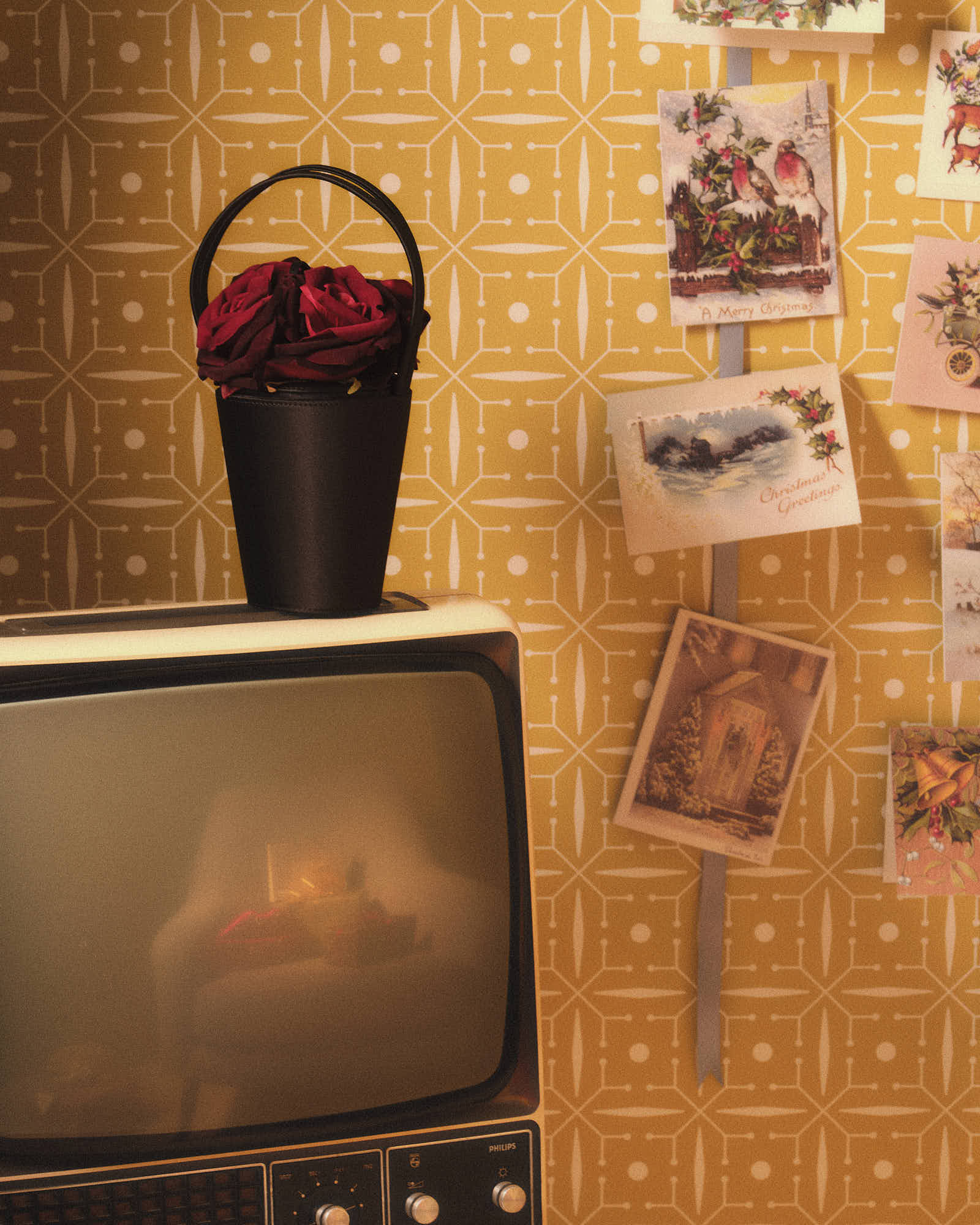 Vintage TV with roses on top, retro wallpaper, and hanging holiday cards.