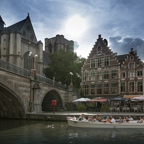 在阳光明媚的天空下，人们乘坐船只游览运河，两岸是历史悠久的建筑和一座石桥。