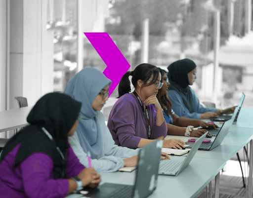 A group of individuals in casual attire actively engages in a workshop, seated at a table with laptops and notepads.