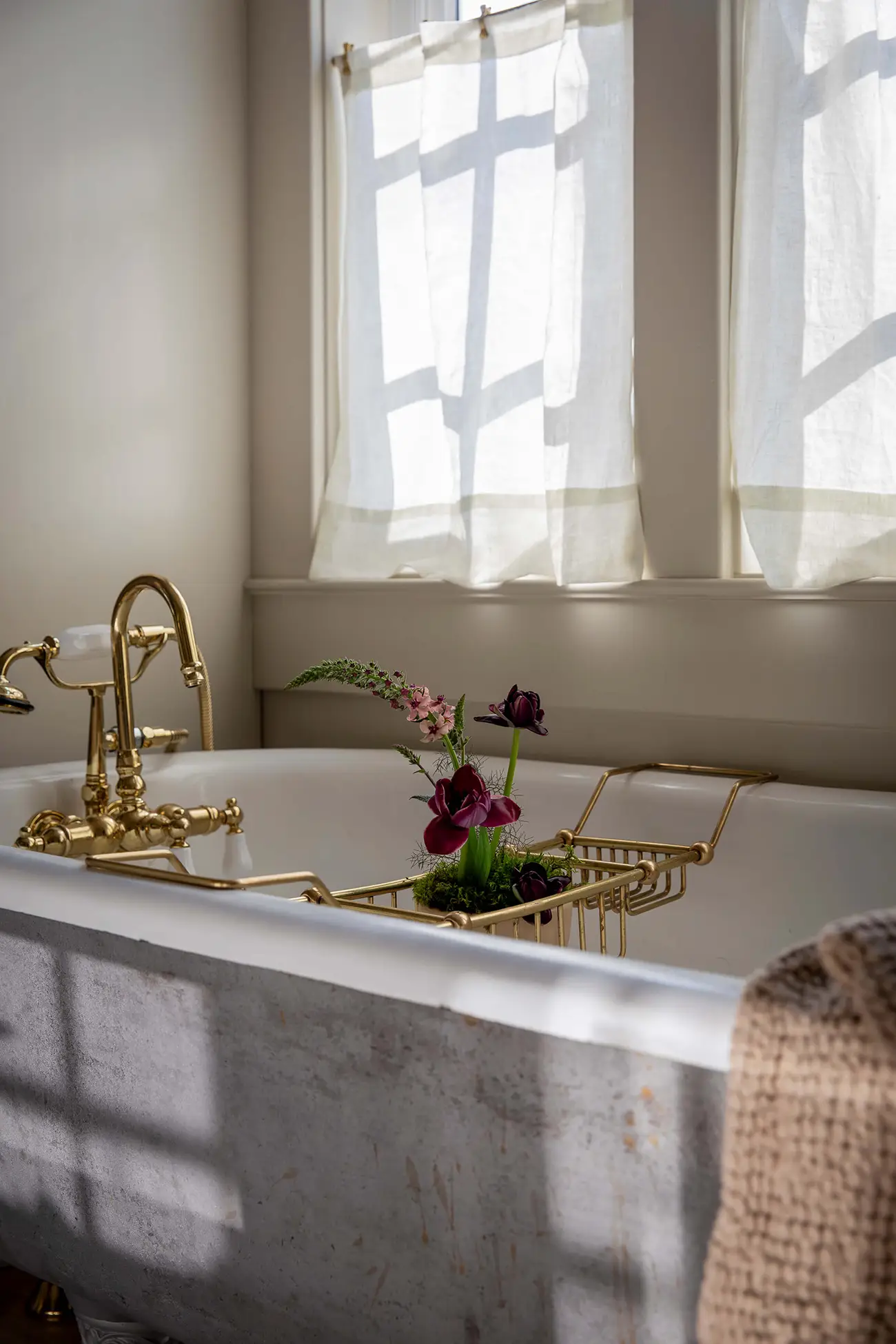 A clawfoot bathtub with a brass faucet in a bathroom of a Hamptons home