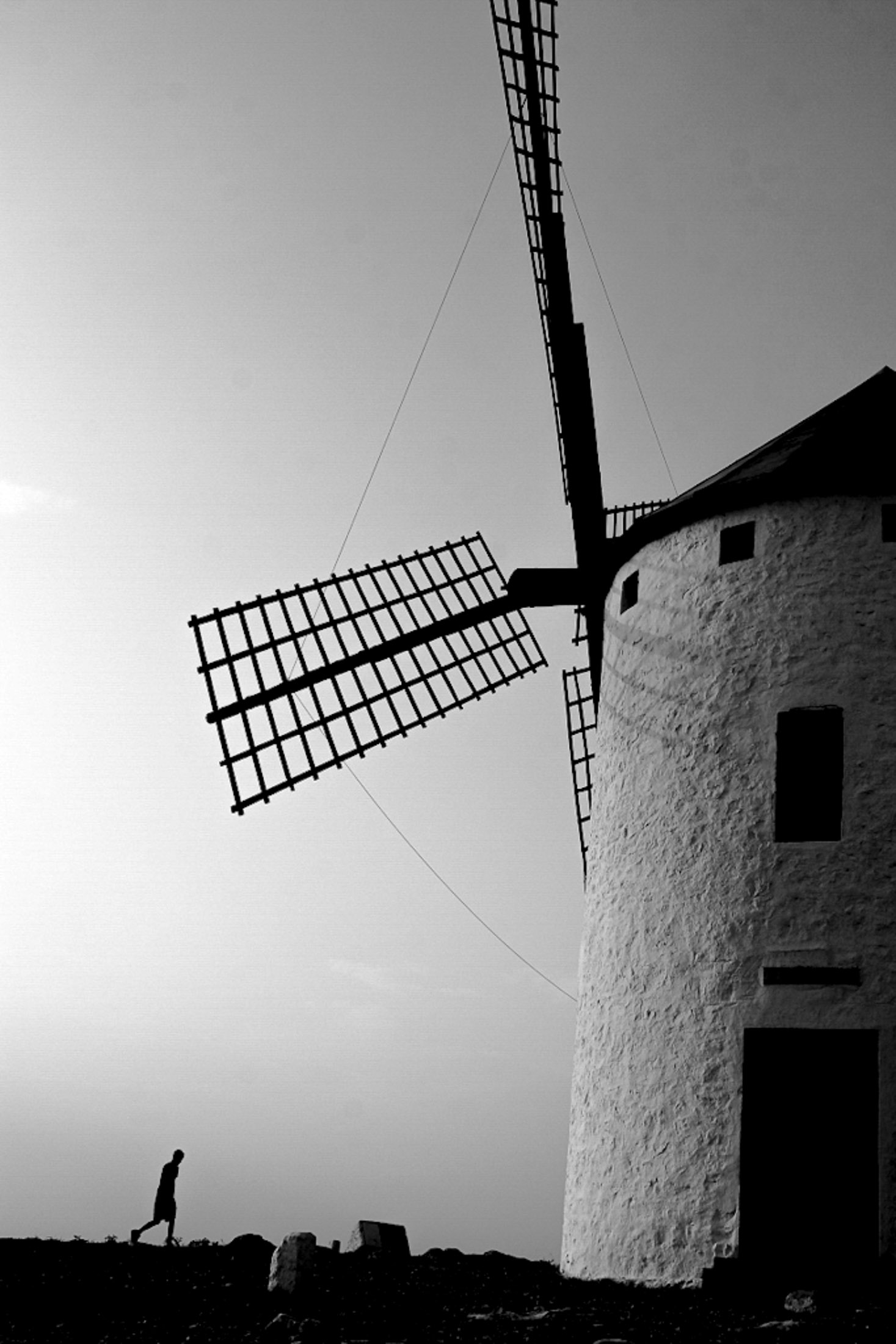 Black and white fine art photograph of a windmill with a solitary figure walking in the foreground
