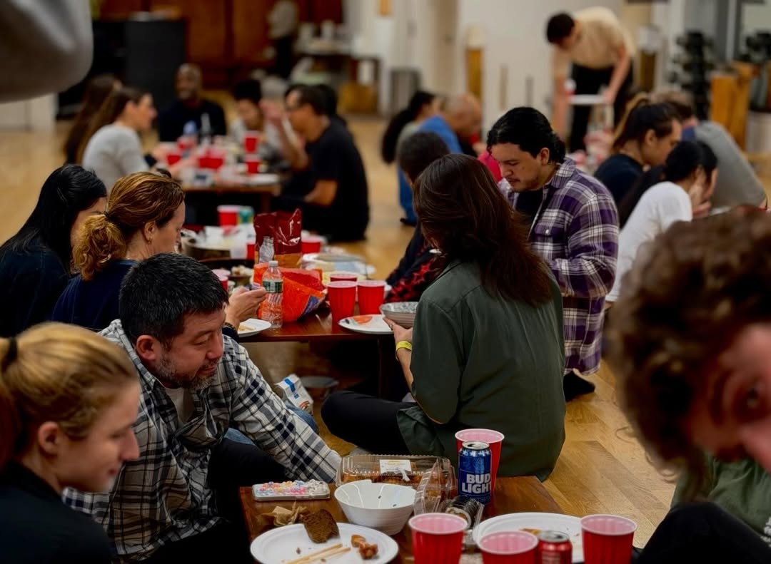 White plate with roasted carrots served on green sauce, topped with almonds and fresh herbs, held by a hand over a dark table.