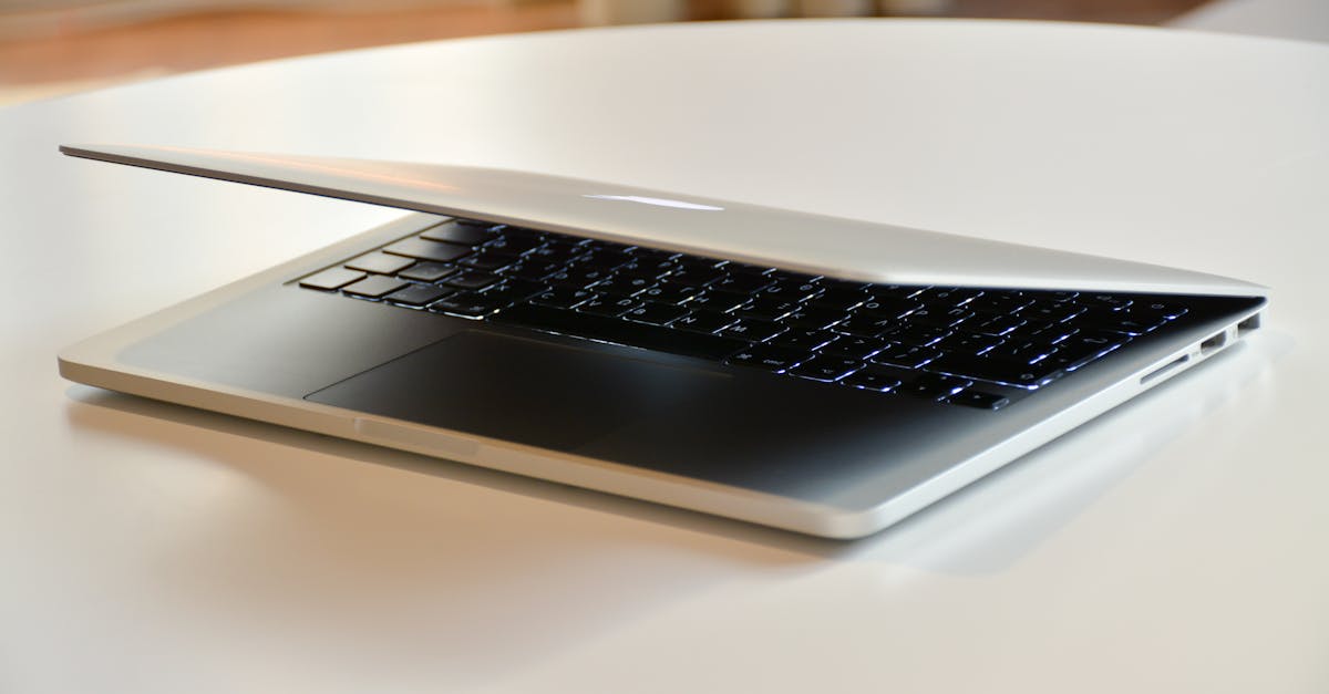 A modern MacBook laptop with a sleek design, slightly closed on a white table indoors.