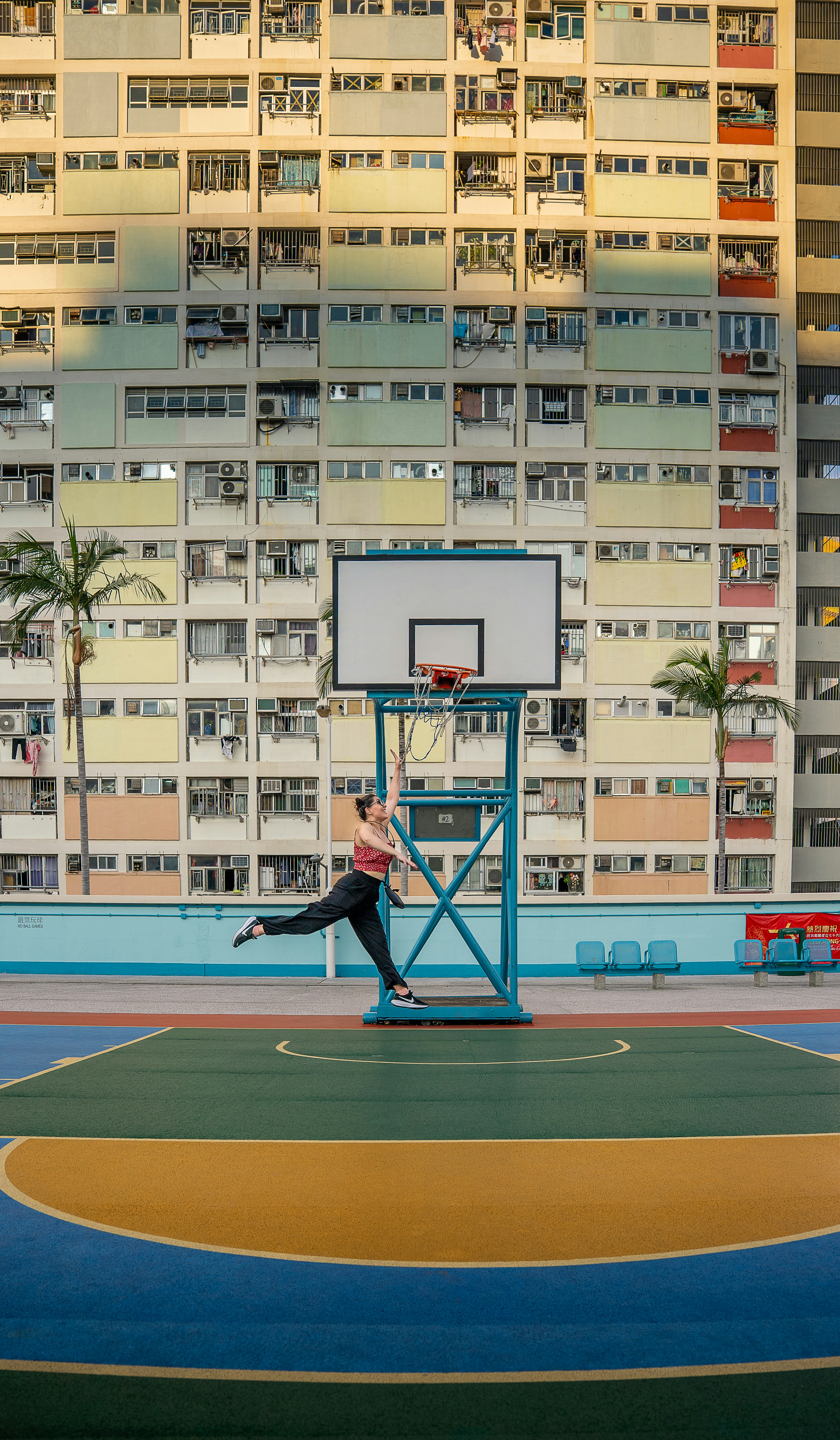 Woman jumping to shoot basketball in front of colorful building