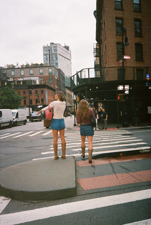 two young women in denim mini skirts walking across the street in the west village