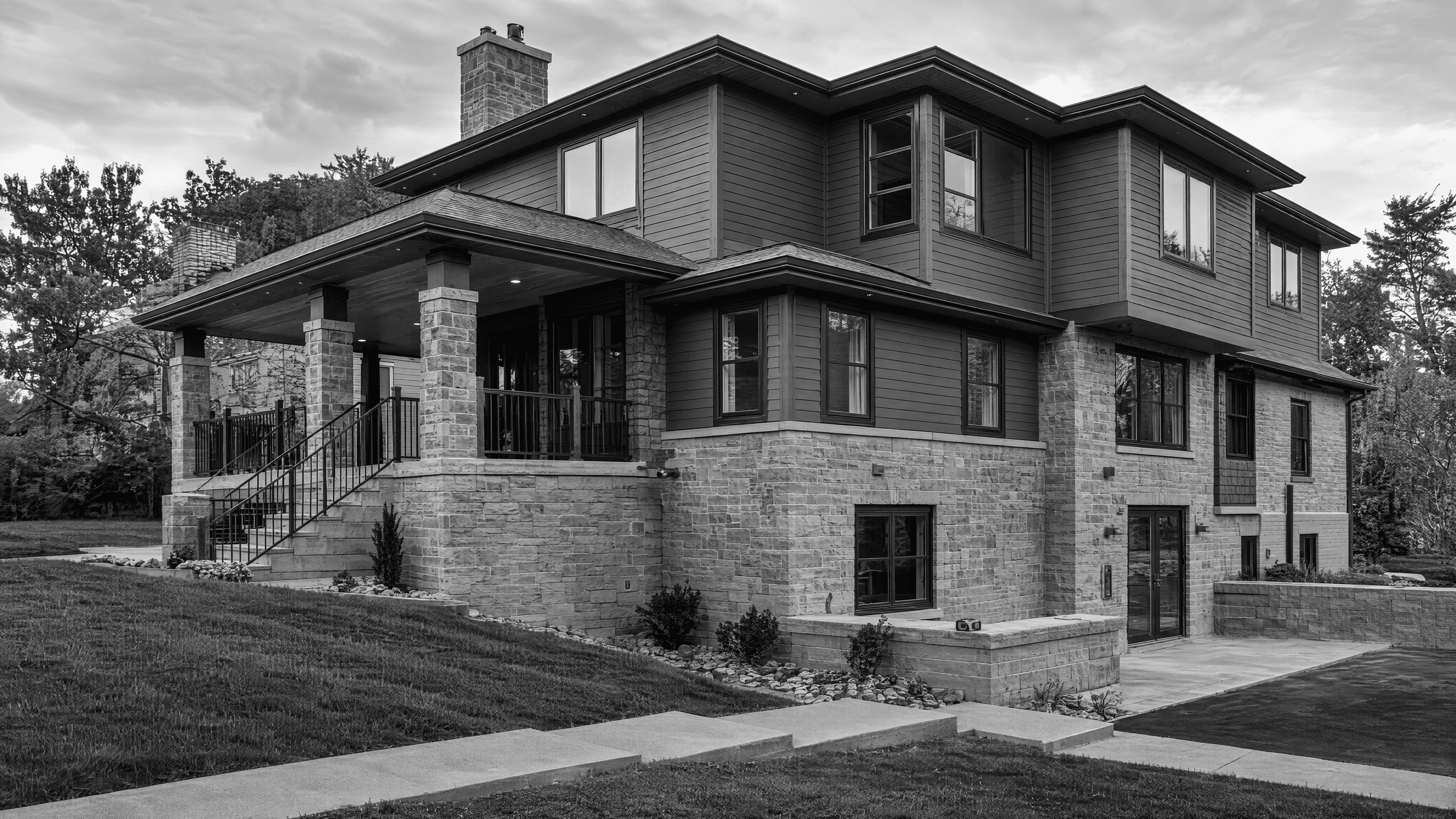 Two-story residence with a stone-clad lower foundation level and basement openings visible along the sloped site.
