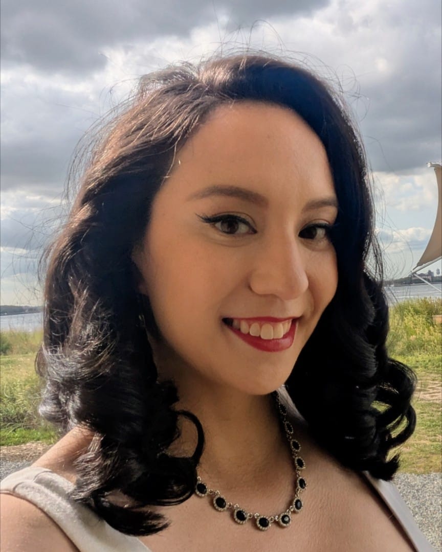 woman in red lipstick smiling in front of a field