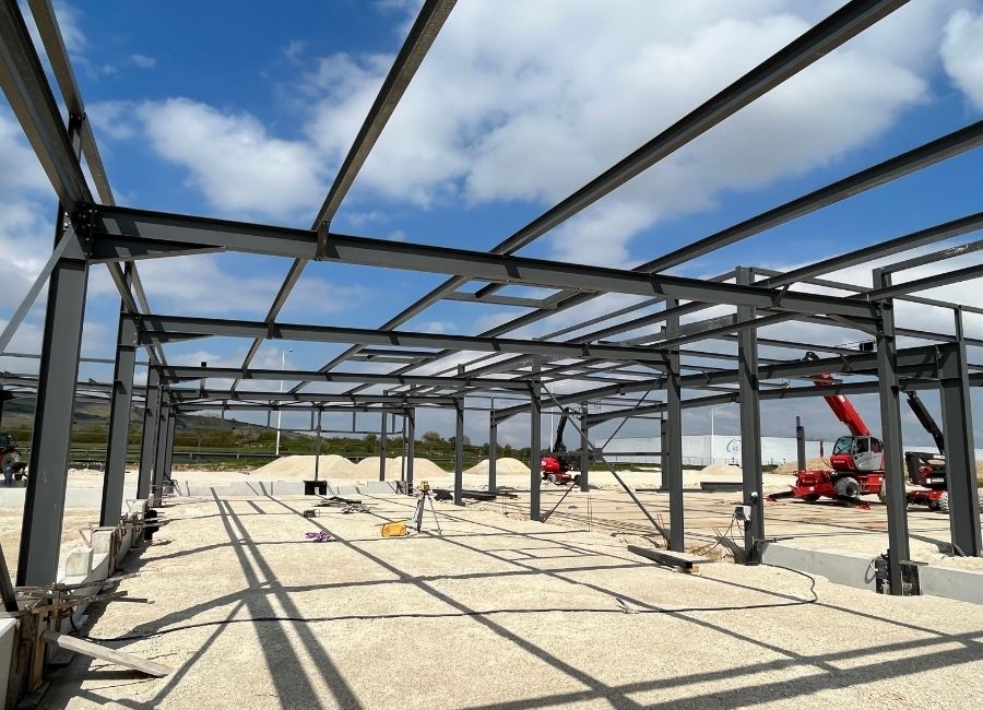 Structure métallique en construction sur un sol sableux, ciel bleu dégagé.