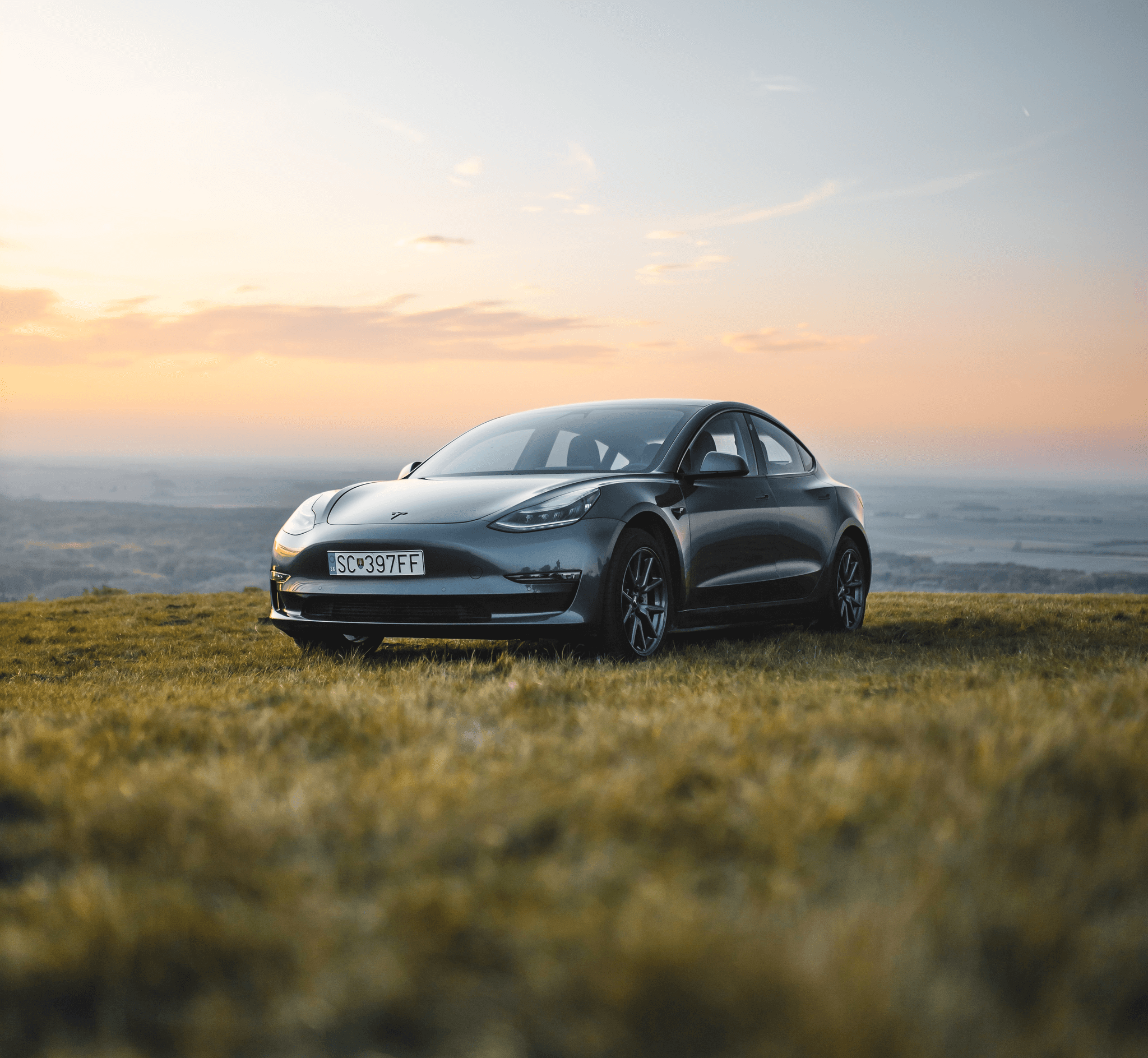 A grey car parked in a grass field in a hilly area