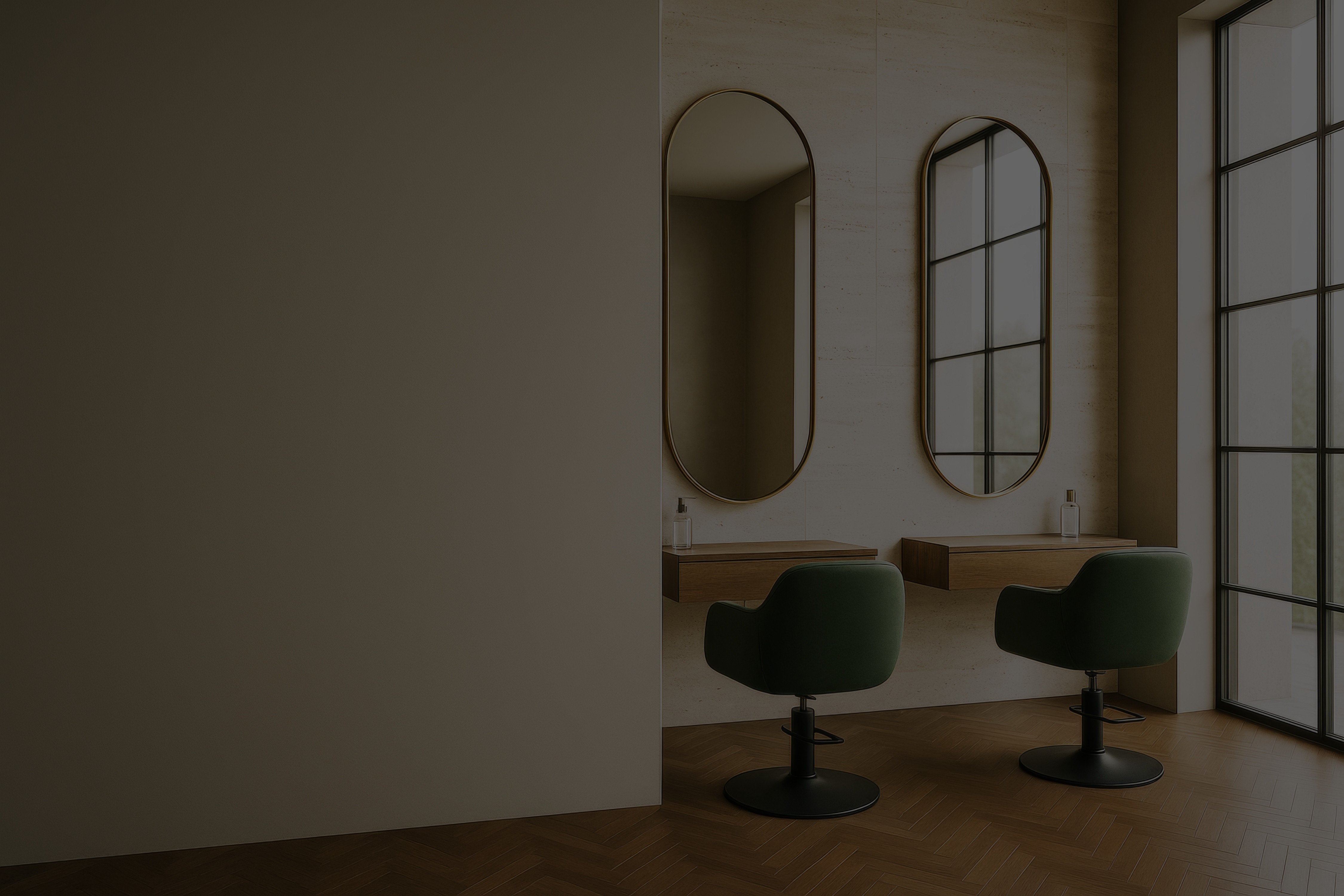 Minimalist hair salon interior with two green styling chairs, oval gold-framed mirrors, floating wood vanity, and natural light from large windows