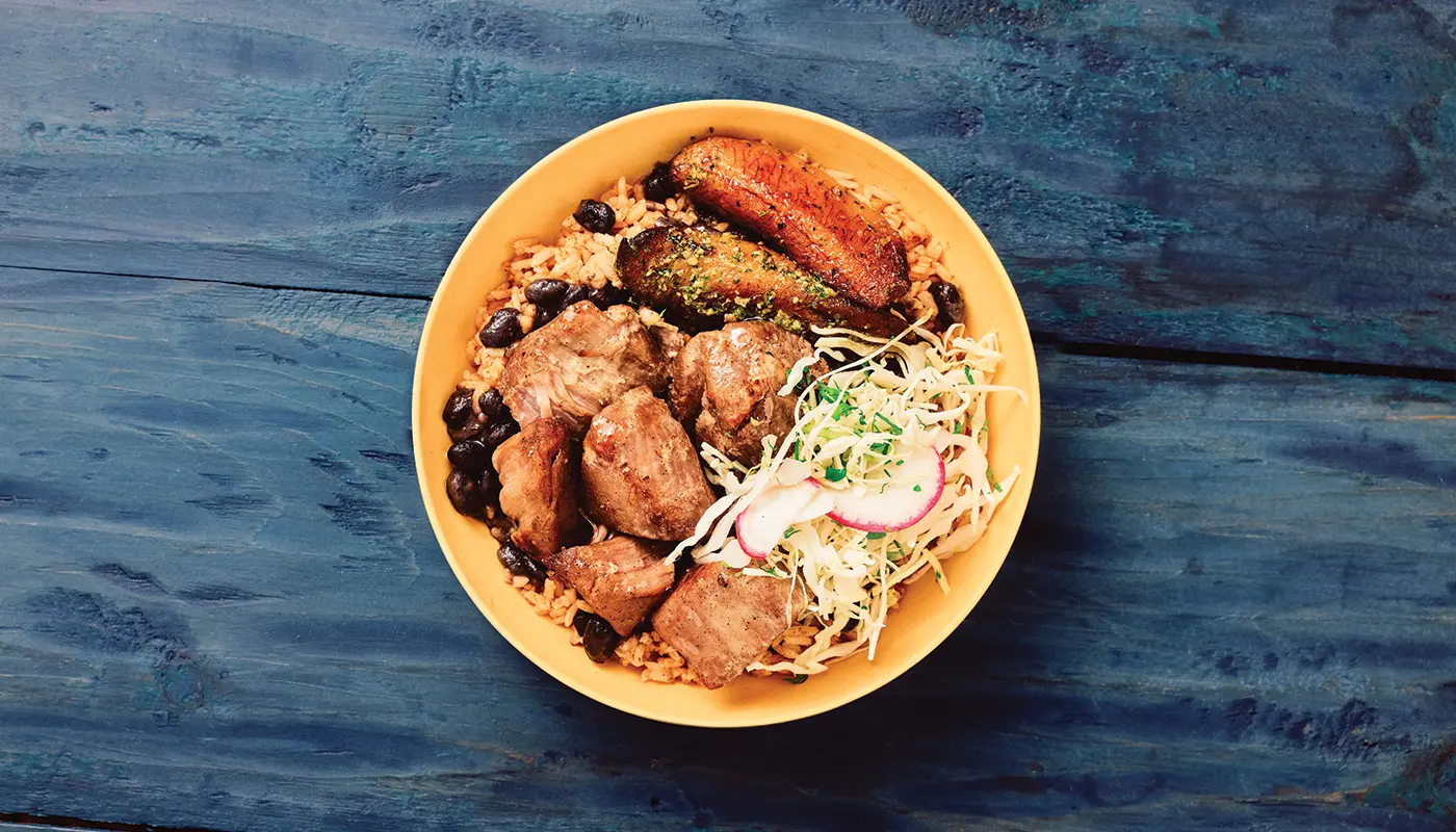 Overhead photograph of the Pernil pork bowl in a yellow bowl on blue wooden boards.