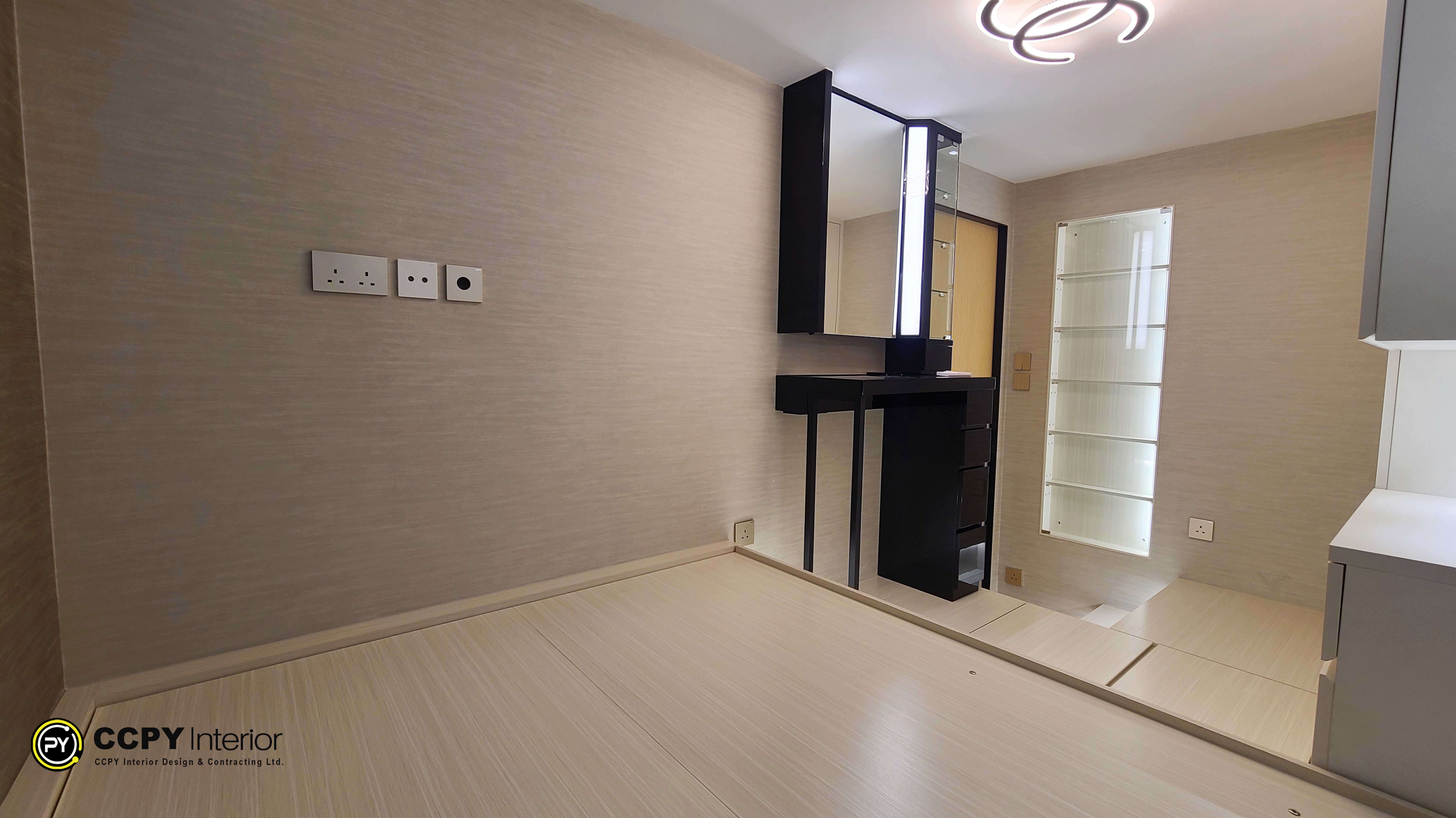 This is a modern bedroom interior designed by CCPY Interior Design featuring a custom storage bed.Storage Solutions: The design includes a specialized lifting storage bed intended to hide suitcases and reduce clutter.Built-in Vanity: A compact, dark-toned vanity with an integrated mirror and lighting is installed against the wall.Lighting and Decor: The space utilizes warm, integrated LED lighting and a neutral color palette of wood, grey, and beige to create a contemporary look.Spatial Efficiency: A large mirror is positioned near the entrance to make the area feel more spacious