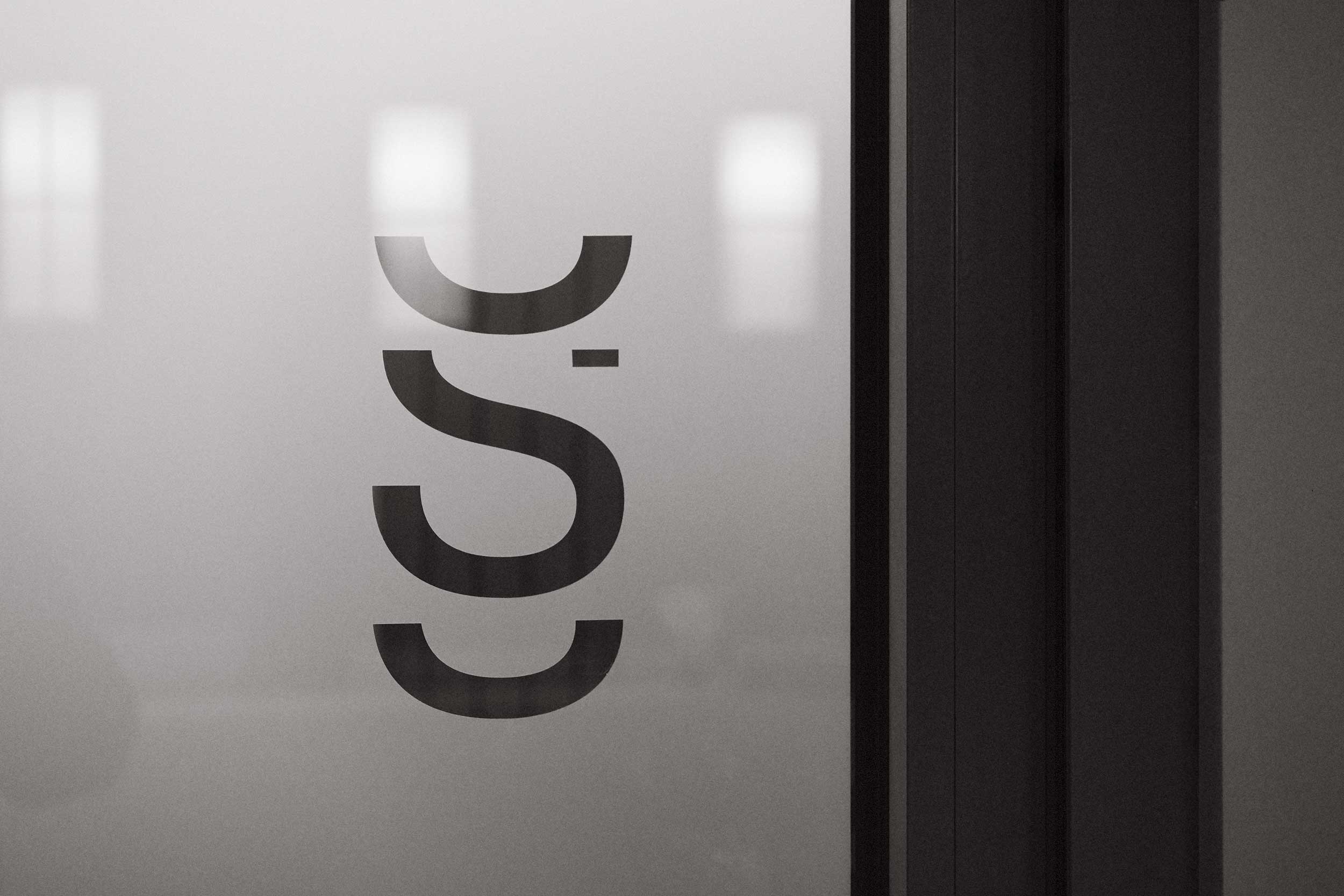 Detailaufnahme einer Milchglas-Tür in der Praxis SpinaMed mit senkrecht platziertem, stilisiertem Logo.