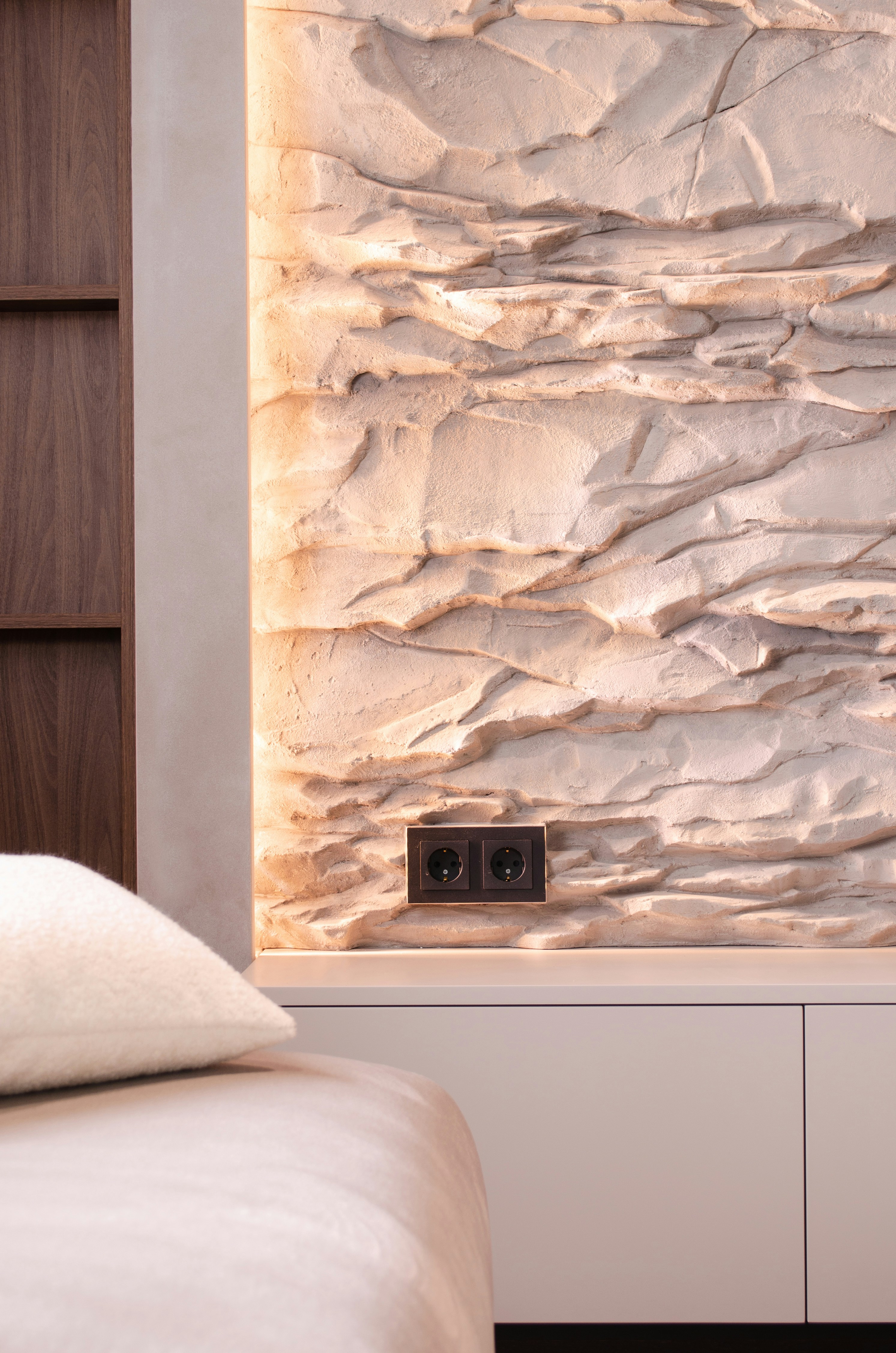 A bedroom with a white bed and a stone wall
