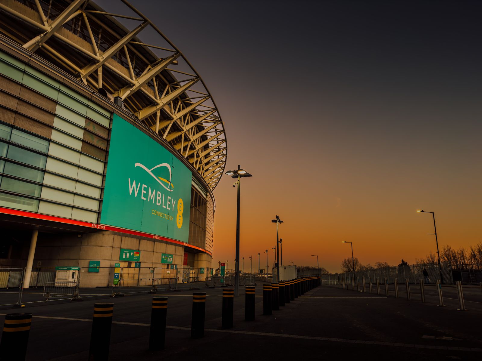 The curved exterior of Wembley Stadium under an orange dawn sky