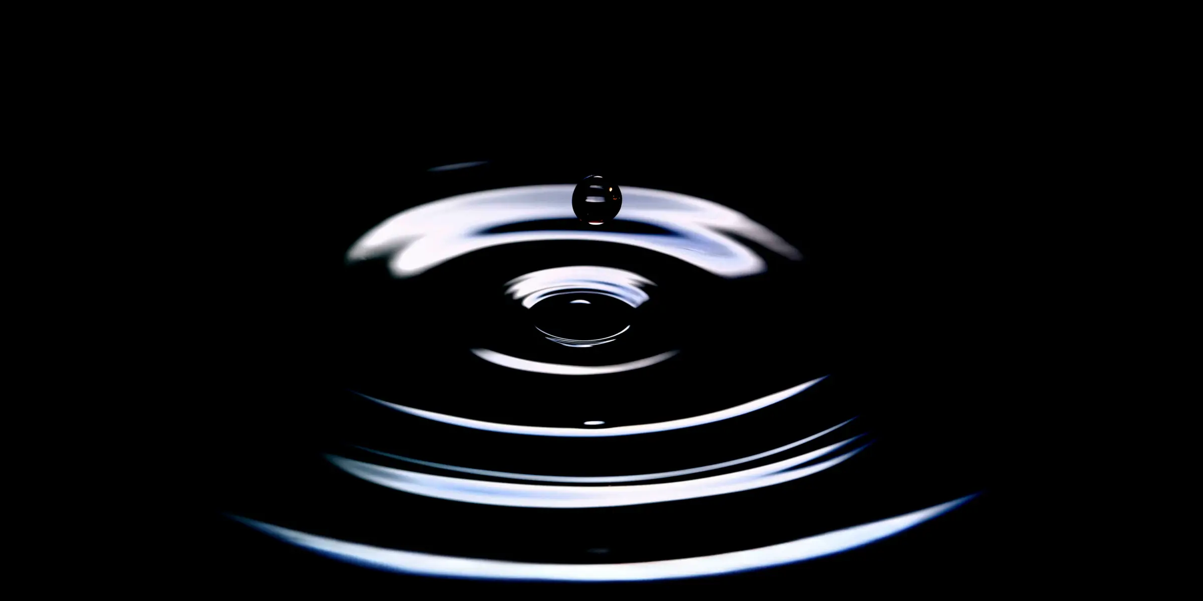 A water droplet captured at the moment it hits a dark surface.