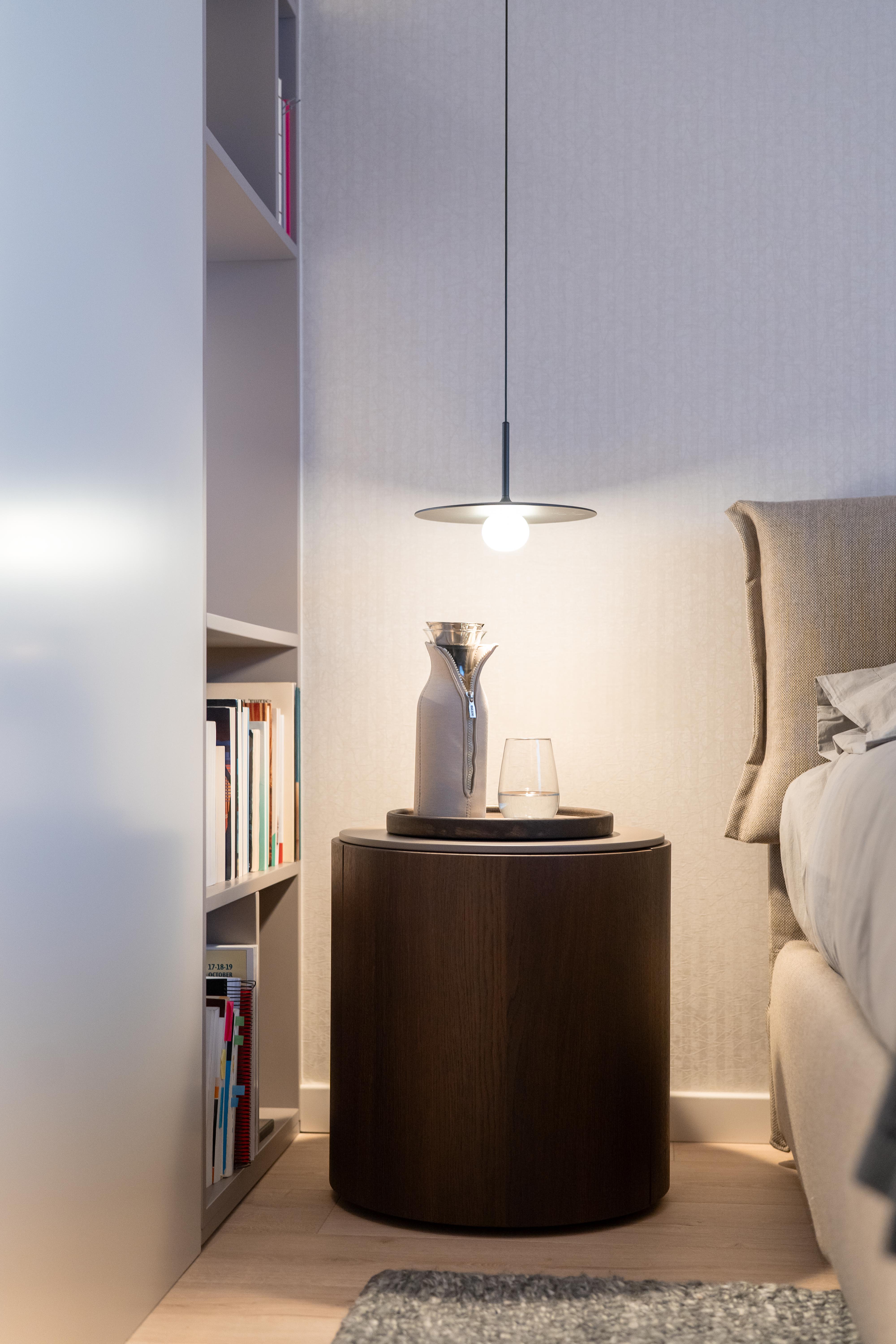 Detalle de mesita de noche cilíndrica con lámpara colgante