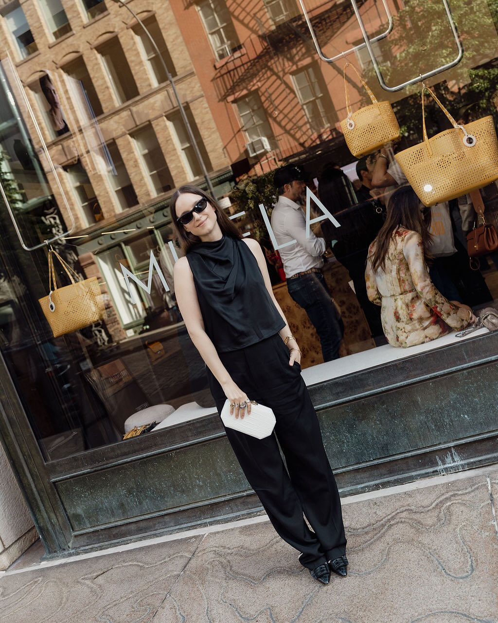 Guest standing outside Misela’s Bond Street boutique during the New York store launch, with suspended handbag window display and vinyl window signage.