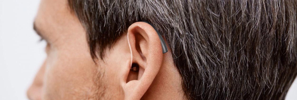 Close-up of a person's ear and short hair, viewed from the side against a neutral background.