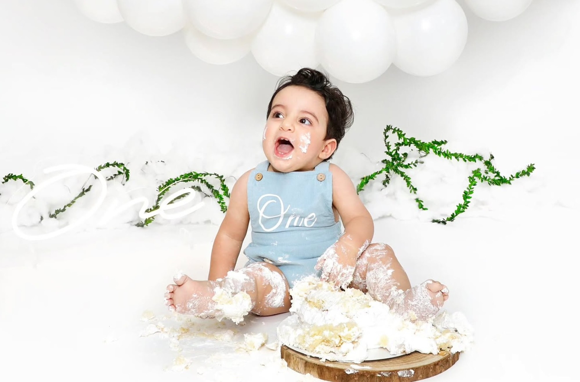 Smiling toddler happily smashing a cream-coloured smash cake during a fun birthday session at Mahvin Photography in Dubai, UAE.