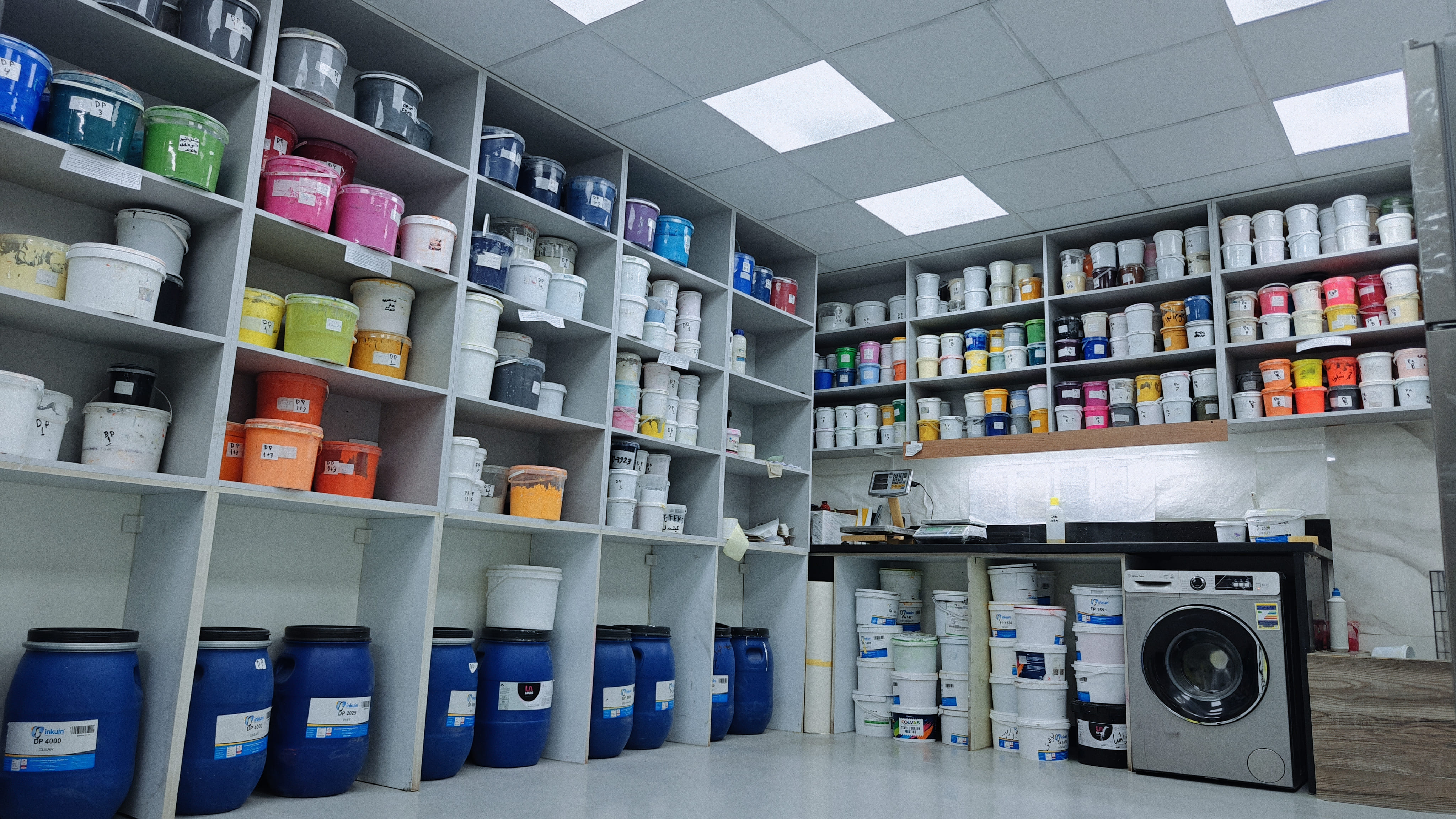Organized textile printing workshop with shelves of ink and dye buckets in various colors.
