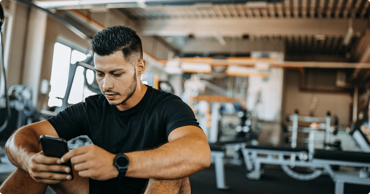 A man in the gym sits in a relaxed position, focused on his phone