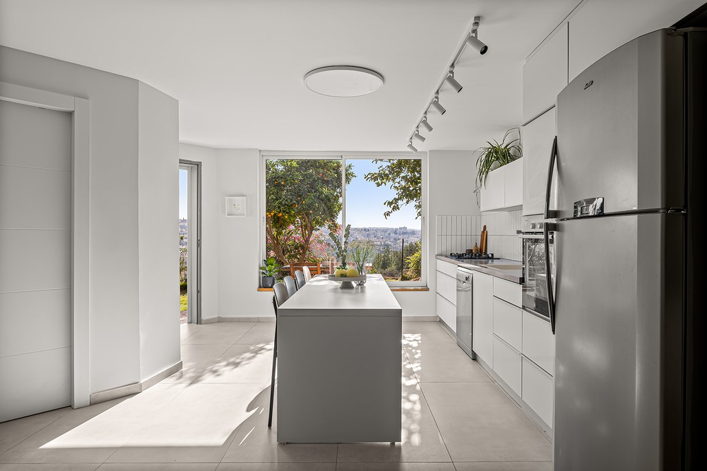 מטבח לבן ומודרני עם חלון גדול הצופה אל נוף אורבני.